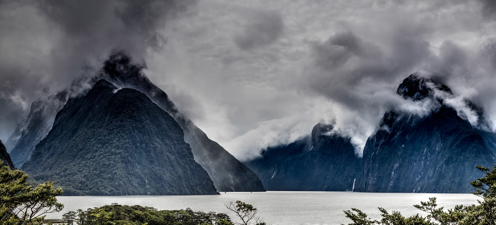 Milford Sound NZ: Milfourd Sound is flanked by 1,683-meter Mitre Peak on the left and the 1,300-meter Lion Peak on the right.  The 151-meter Stirling Falls exits a hanging valley at the foot of Lion Peak.