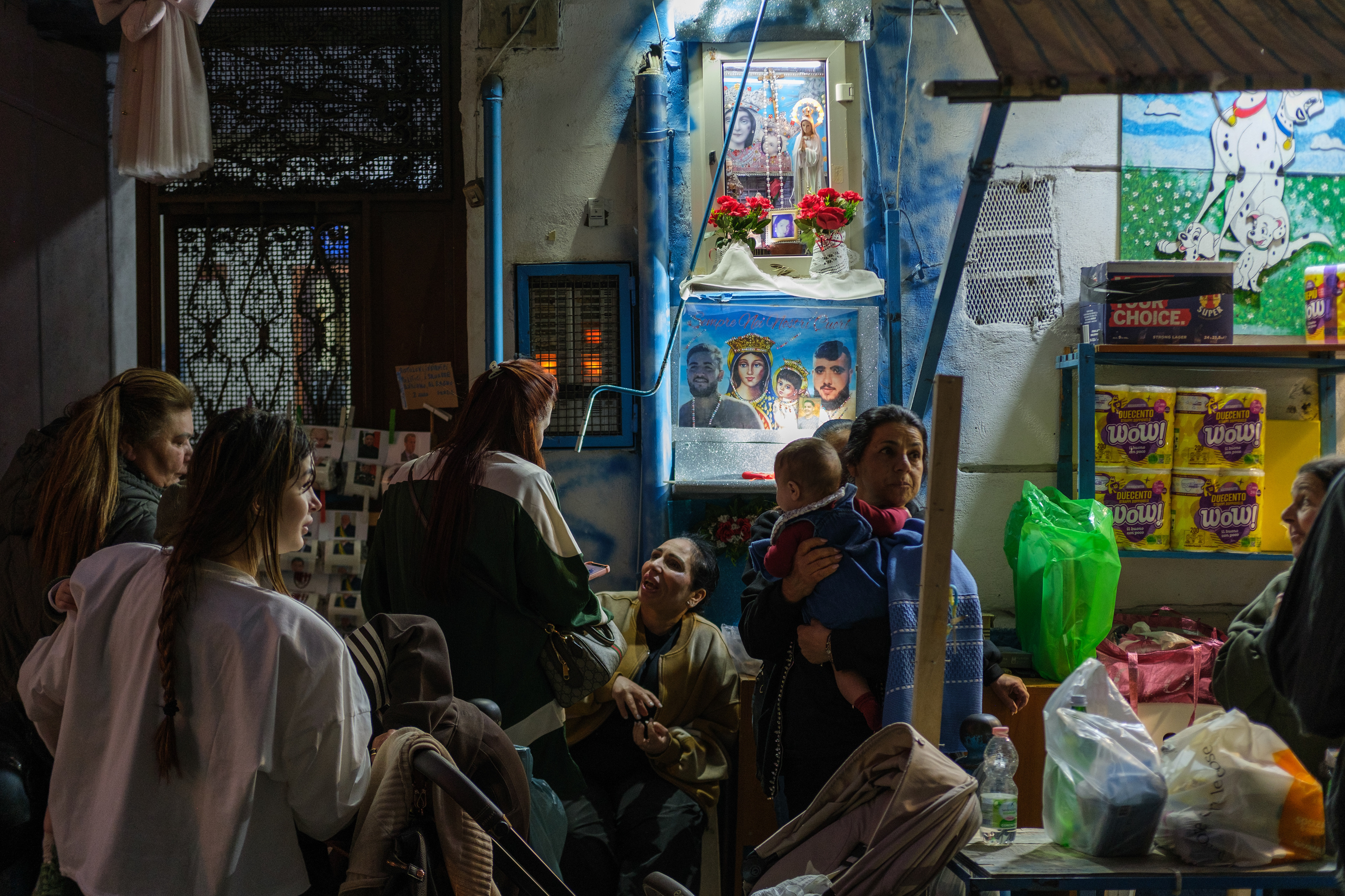 Naples (Italy): Residents gather on a neighborhood street in the Rione Sanità district, next to an illuminated edicola votiva (street shrine) decorated with flowers and photographs. 