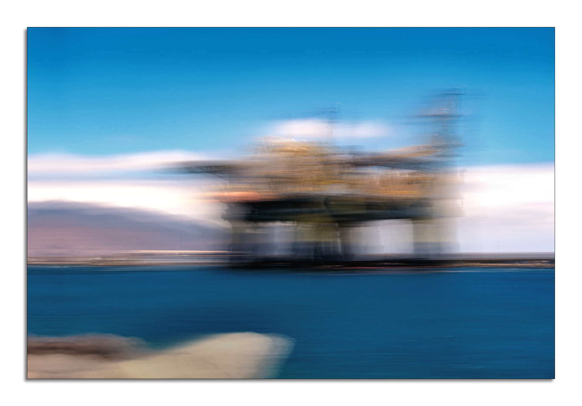 Energie in Bewegung Bildbeschreibung (ALT-Text): Ein abstraktes Foto, das durch beabsichtigte Kamerabewegung (ICM) entstanden ist und eine Ölplattform oder eine große Hafenanlage im Meer darstellt. Der Himmel und das Wasser sind in leuchtenden Blautönen gehalten, während die zentrale Struktur und die Berge im Hintergrund durch die Bewegung zu dynamischen, horizontalen Streifen aus Gelb-, Braun- und Weißtönen verschwimmen. Die Szene vermittelt ein Gefühl von Geschwindigkeit und Energie und hat eine fast malerische Qualität. Hashtags für Instagram: #abstraktefotografie #fotokunst #icm_photography #intentionalcameramovement #bewegungsunschärfe #langzeitbelichtung #küstenliebe #hafen #industriekultur #modernart #artofvisuals #impressionistisch #seascape #energieinbewegung #kreativefotografie
