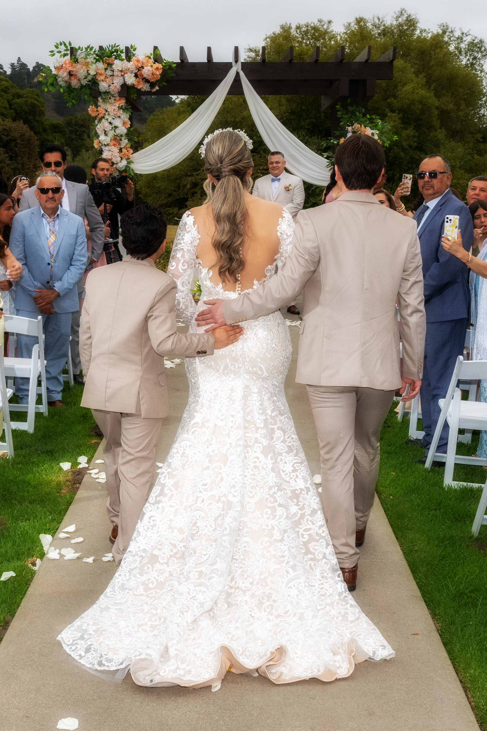 The bride, escorted by her two young sons, during a heartfelt ceremony at Carmel Fields by Wedgewood Weddings, captured by Monterey Photography — a timeless moment in Carmel Valley.
