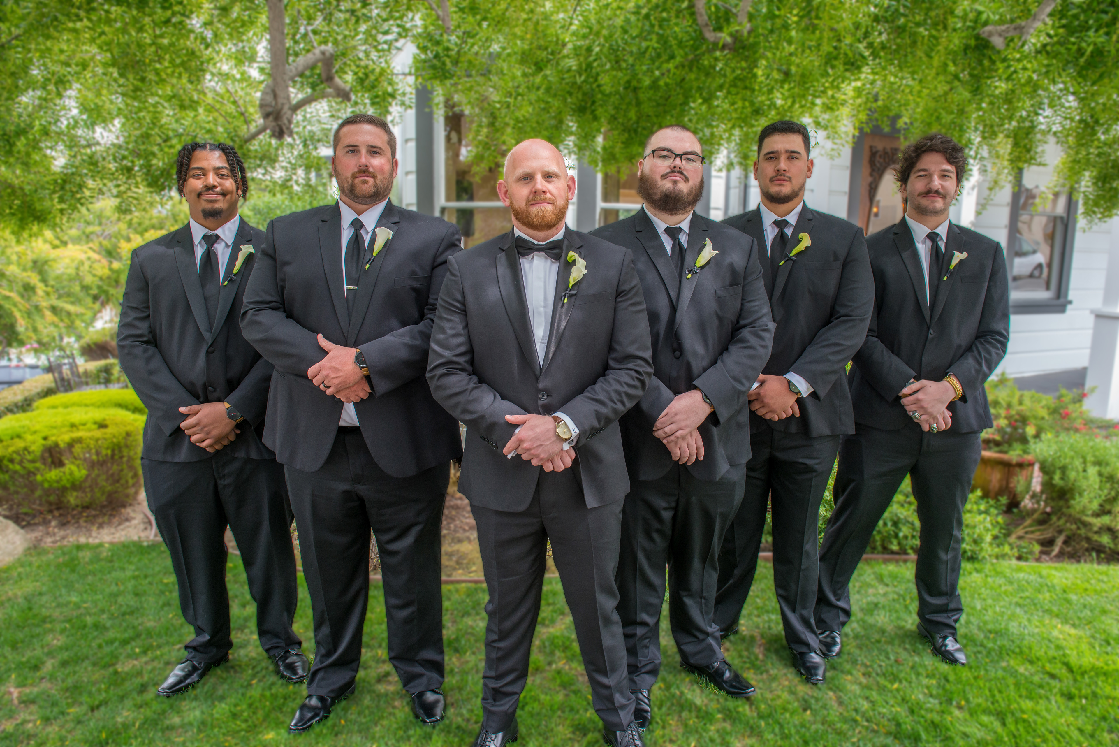 A groom and his groomsmen stand together in front of The Perry House in Monterey, CA. The groom is smiling, looking confident and happy, while his groomsmen surround him, sharing a moment of camaraderie and joy. The historic Victorian architecture of The Perry House serves as a beautiful backdrop, adding elegance and charm to the scene.