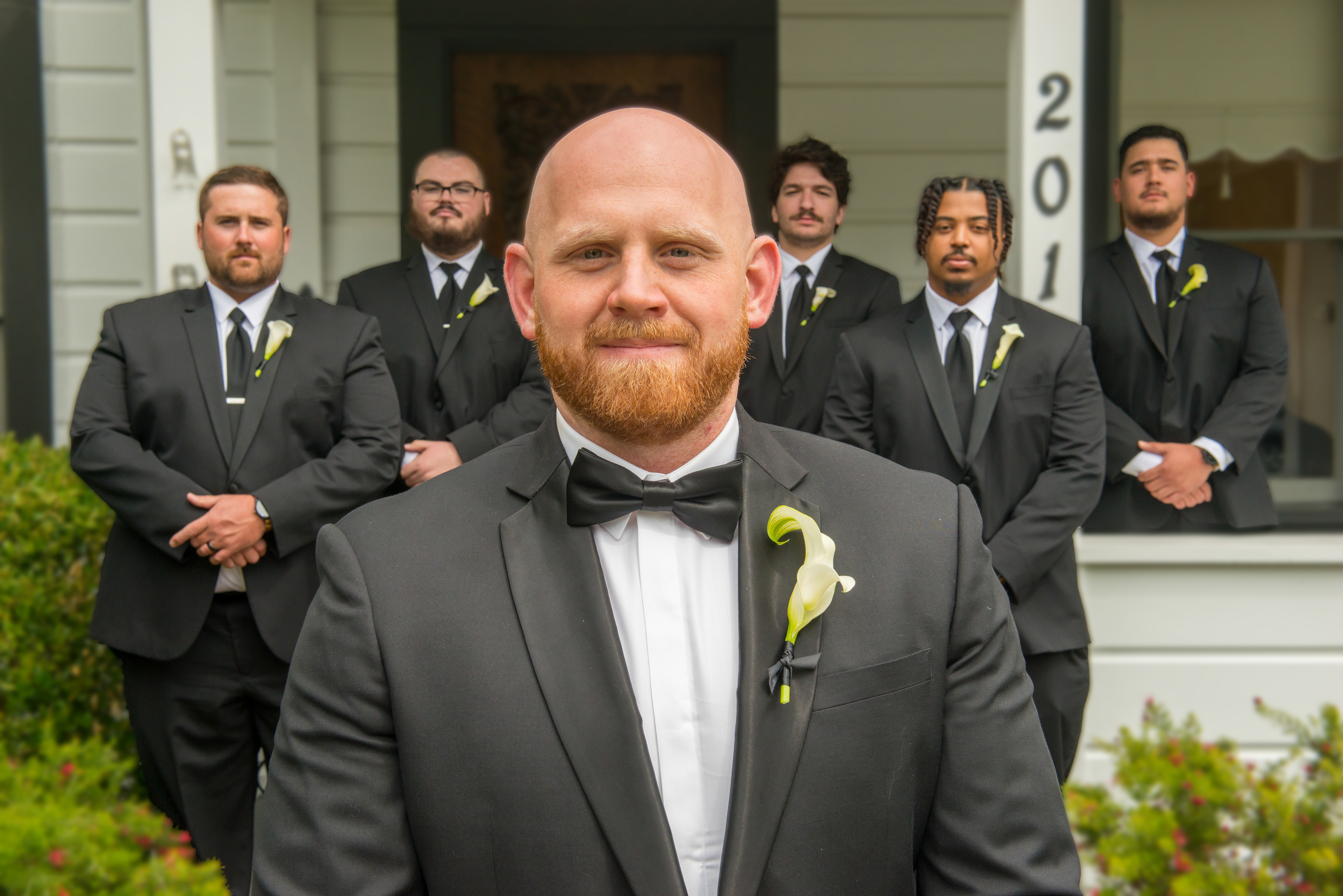 A groom and his groomsmen stand together in front of The Perry House in Monterey, CA. The groom is smiling, looking confident and happy, while his groomsmen surround him, sharing a moment of camaraderie and joy. The historic Victorian architecture of The Perry House serves as a beautiful backdrop, adding elegance and charm to the scene.