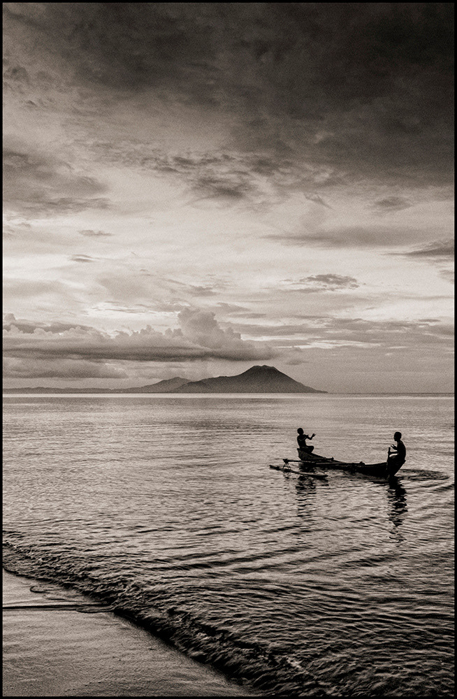 Boys in an out-rigger canoe (Tavurvur & Vulcan Volcanoes in the background), Kokopo Beach, Kokopo, East New Britain
