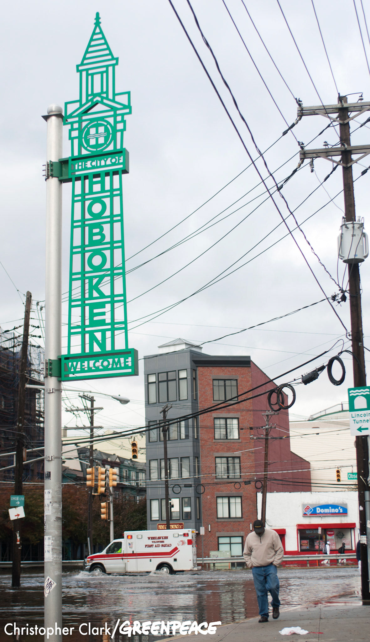 A sign welcoming visitors to the city of Hoboken looms over a passing man and ambulance in the flooded streets of Hoboken, New Jersey in the aftermath of hurricane Sandy on October 31st, 2012.