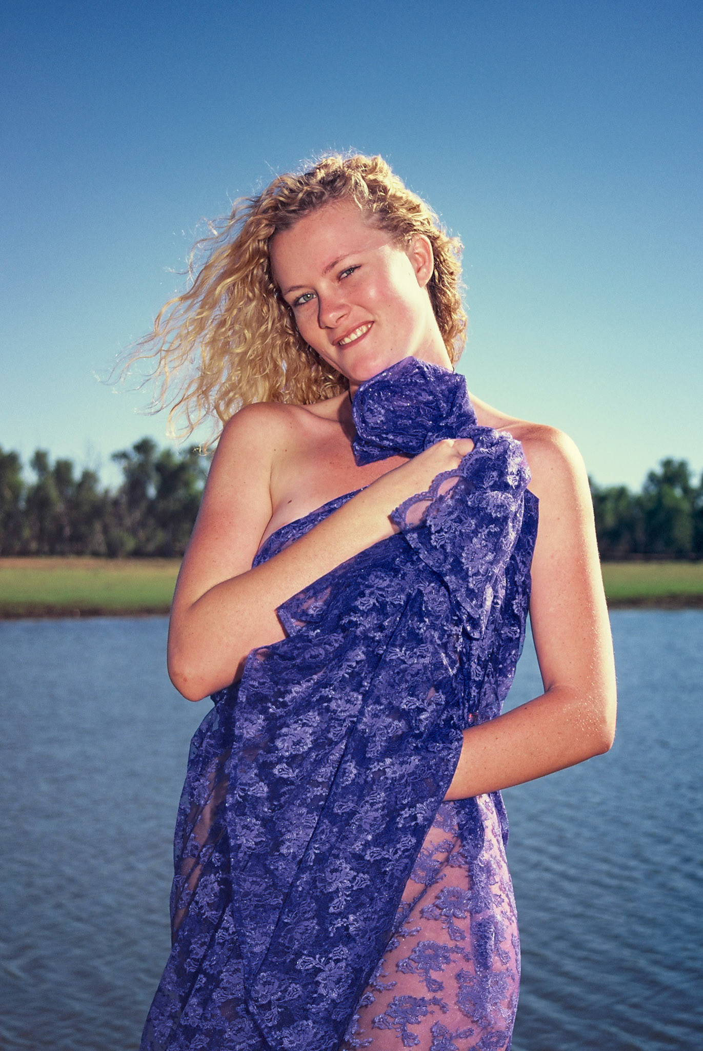 young lady in draped blue lace lake edge enjoying sunshine lake side curly blond hair