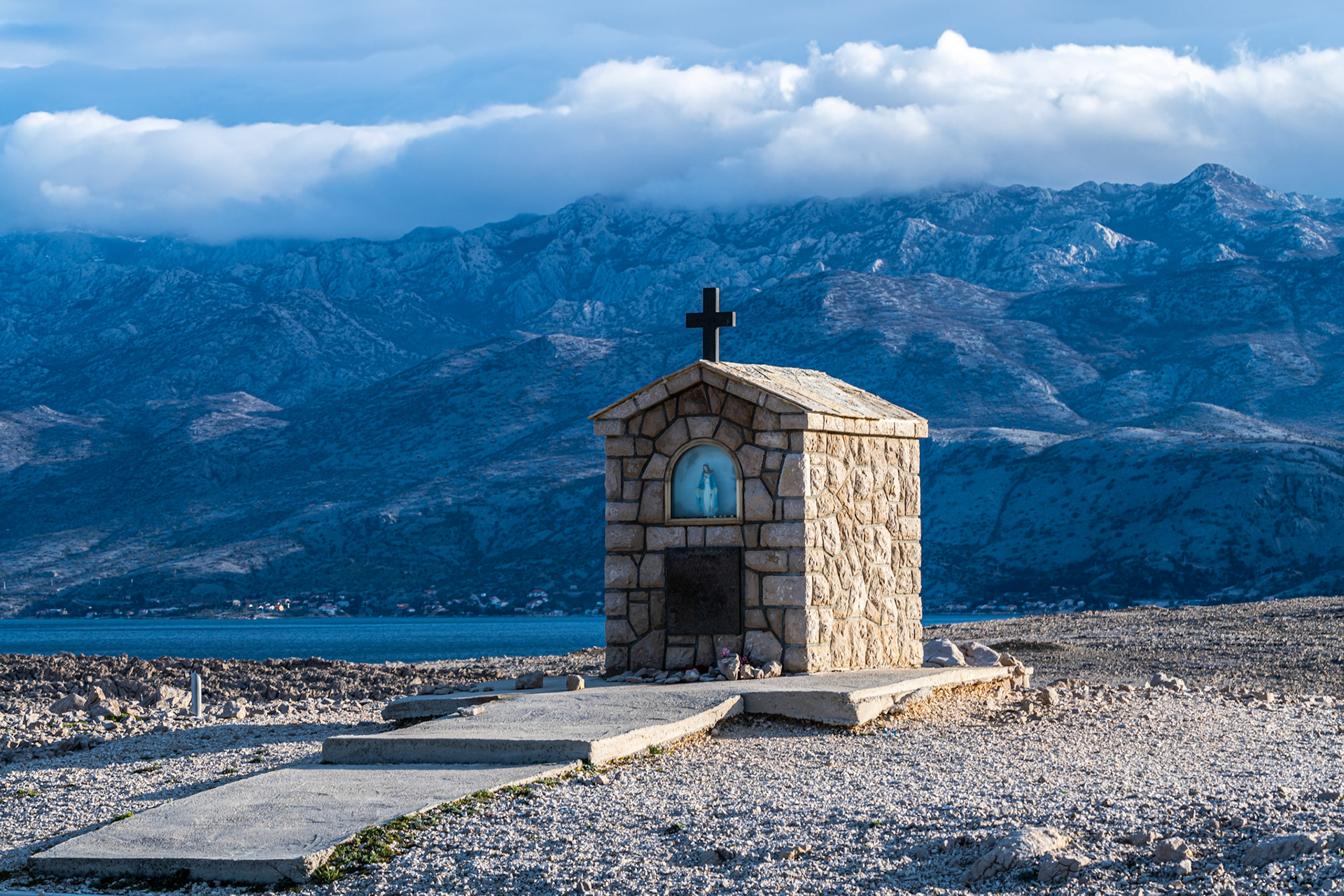 Morning light illuminates this church on the Island of Pag, with the mainland's Velebit mountains looming