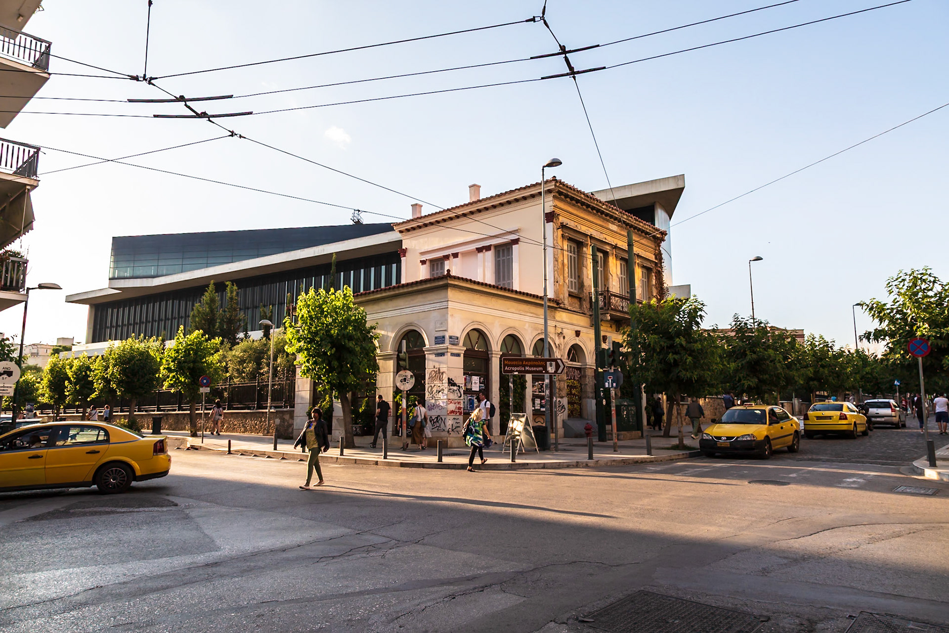 Athens, Greece - May 23rd 2018: Pedestrians cross the street near the Acropolis Museum, while yellow taxis wait for passengers, showcasing daily life in Athens.