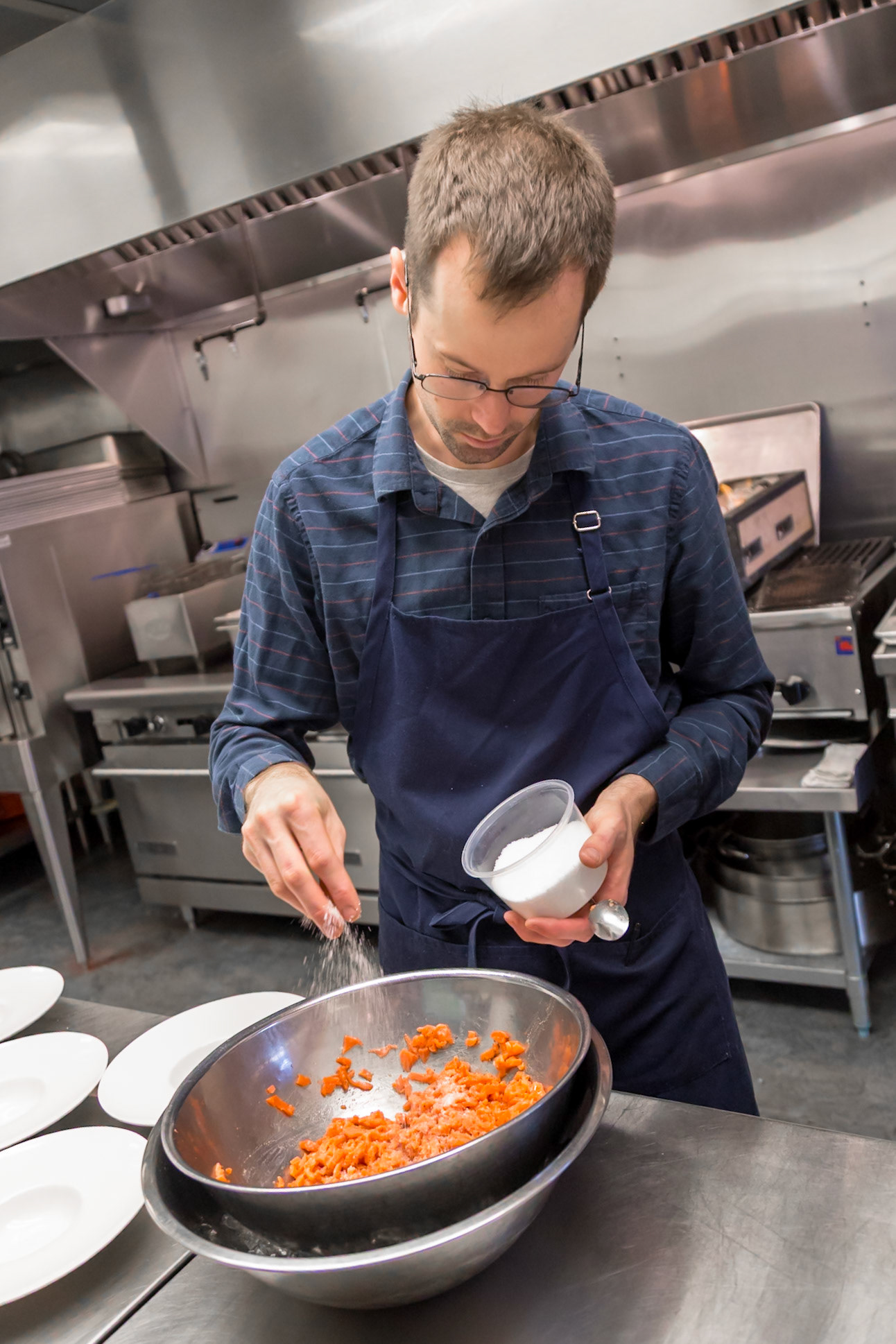 Fog Lark, Portland, Oregon - April 6th 2018: A chef seasons diced salmon in a commercial kitchen, preparing it for a dish.