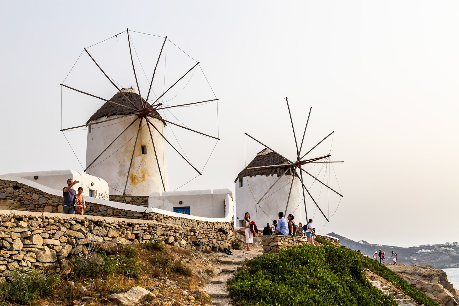 Mykonos, Greece - May 23rd 2018: Tourists visit the iconic windmills, a popular attraction, to enjoy the views and capture photos.