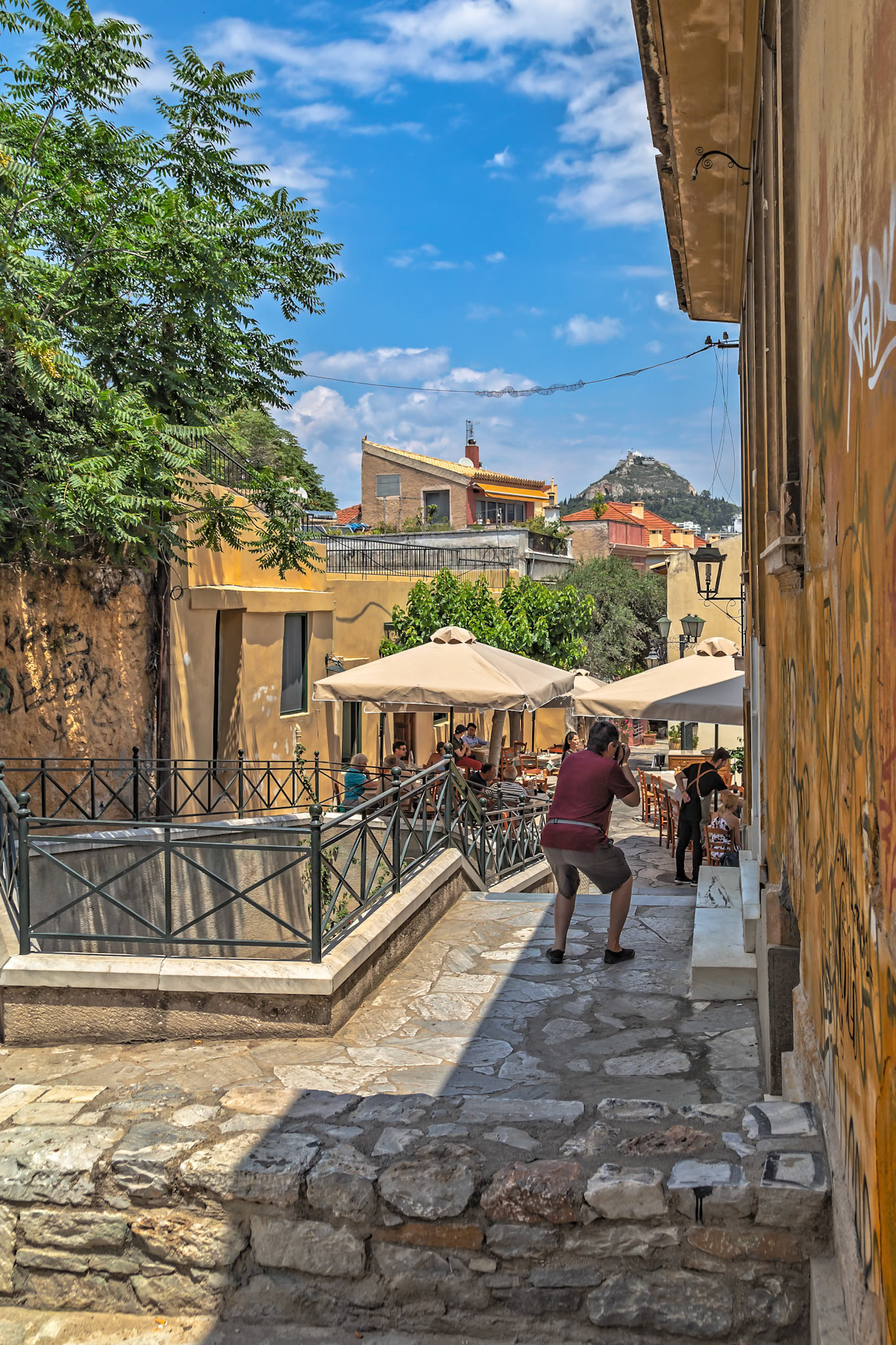 Athens, Greece - May 23rd 2018: A tourist takes a photo of a couple sitting at a cafe in the Plaka district, capturing the essence of Greek life.