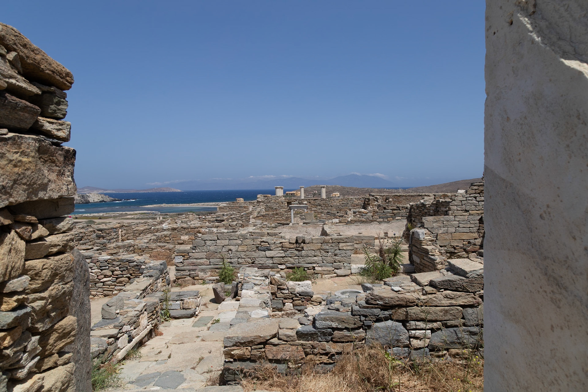 Delos, Greece - May 22nd 2018: Ruins of ancient buildings stand against a clear blue sky and sea, showcasing the historical significance of Delos.