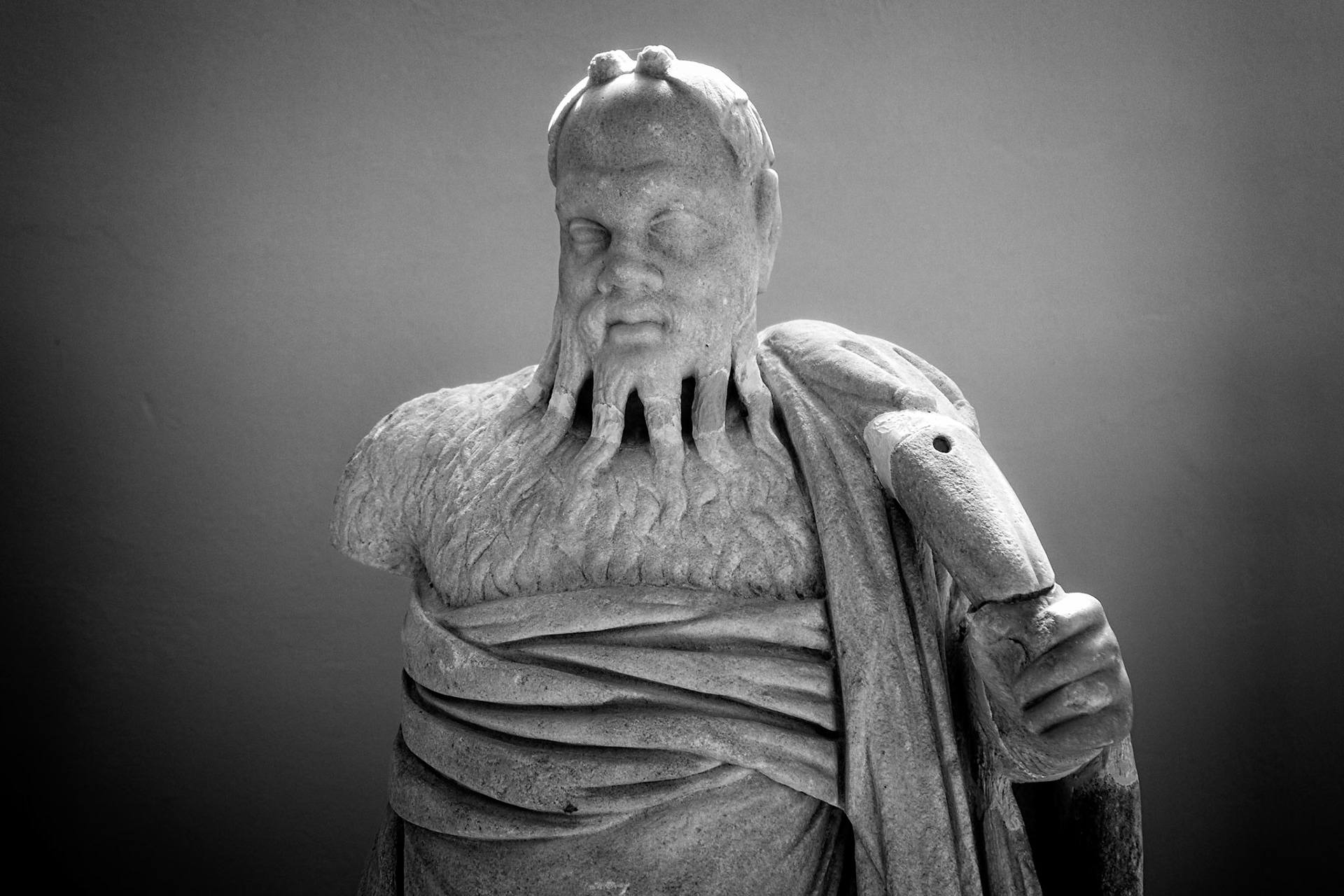 Delos, Greece - May 22nd 2018: A black and white image of a weathered statue of Poseidon, the Greek god of the sea, stands as a testament to ancient artistry.