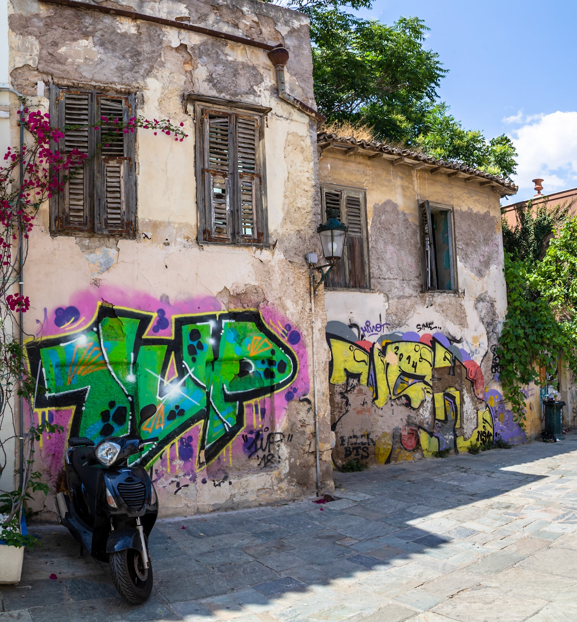 Athens, Greece - May 23rd 2018: A black scooter is parked in front of a graffiti-covered building. The graffiti is likely art, or vandalism.