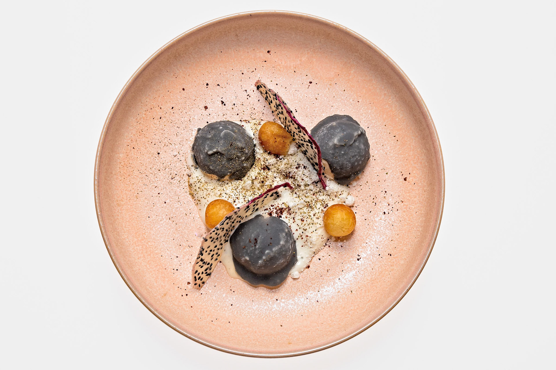 Fog Lark, Portland, Oregon - March 15th 2019: A culinary artist plates a modern dish with dark dumplings, fried spheres, and dragon fruit.