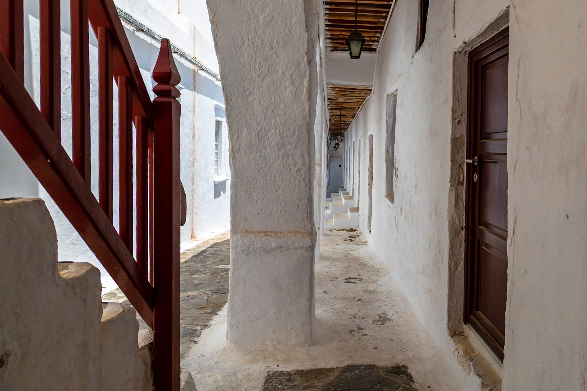 Mykonos, Greece - May 22nd 2018: A view of a traditional whitewashed alleyway with a red wooden railing in the foreground.