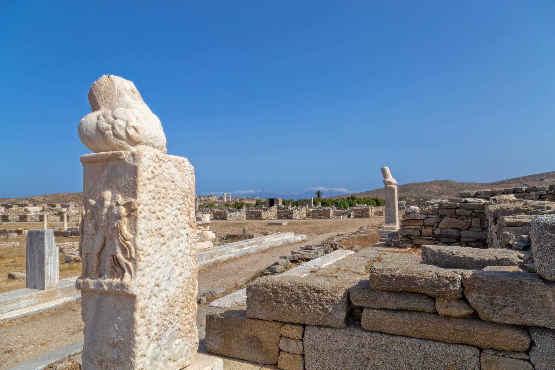 Delos, Greece - May 22nd 2018: Ruins of ancient Delos, a sacred island in Greek mythology, with stone structures and artifacts under a clear blue sky.