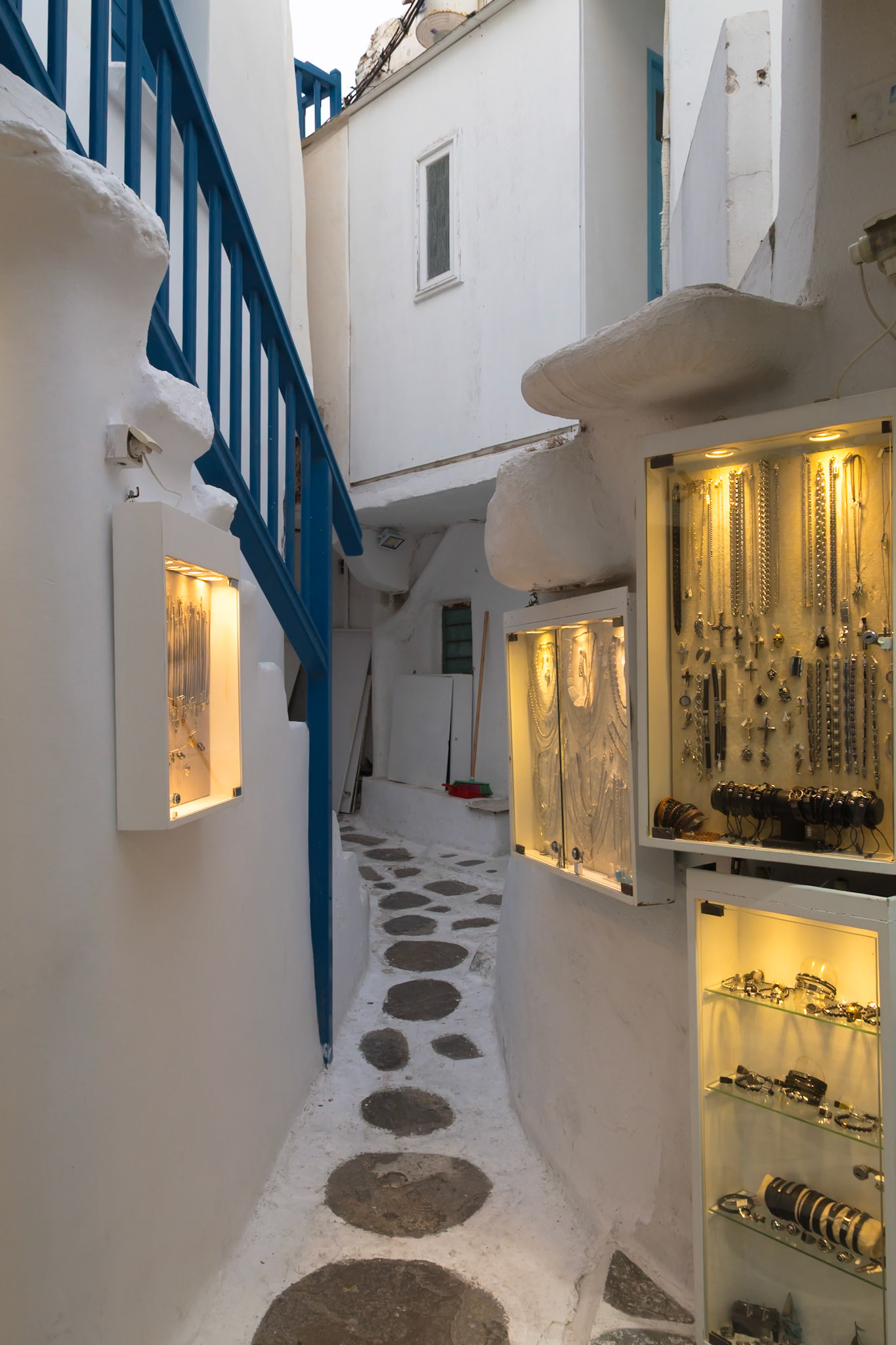 Mykonos, Greece - May 23rd 2018: A narrow street displays jewelry in lit cases, enticing tourists to shop in this picturesque location.