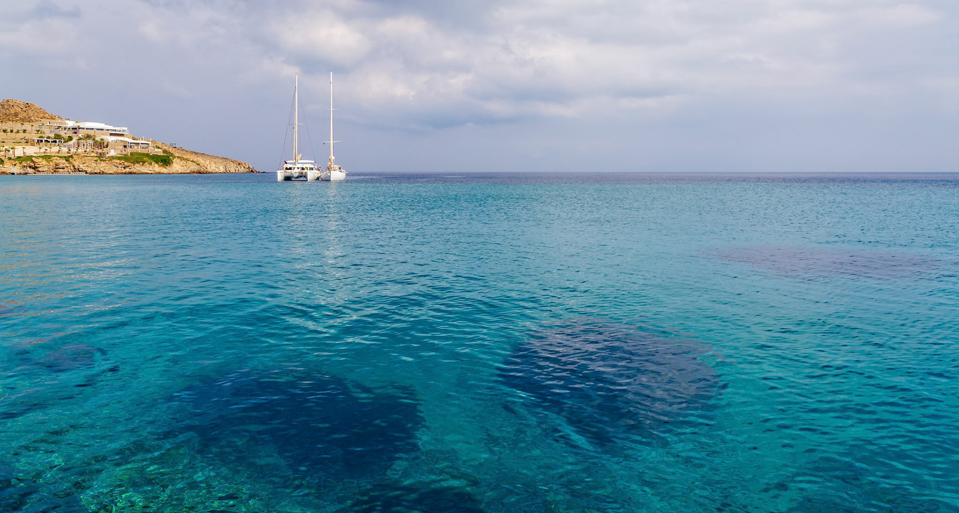 Paradise Beach, Mykonos, Greece - May 24th 2018: Two catamarans are anchored in the clear turquoise water off the coast of Mykonos.