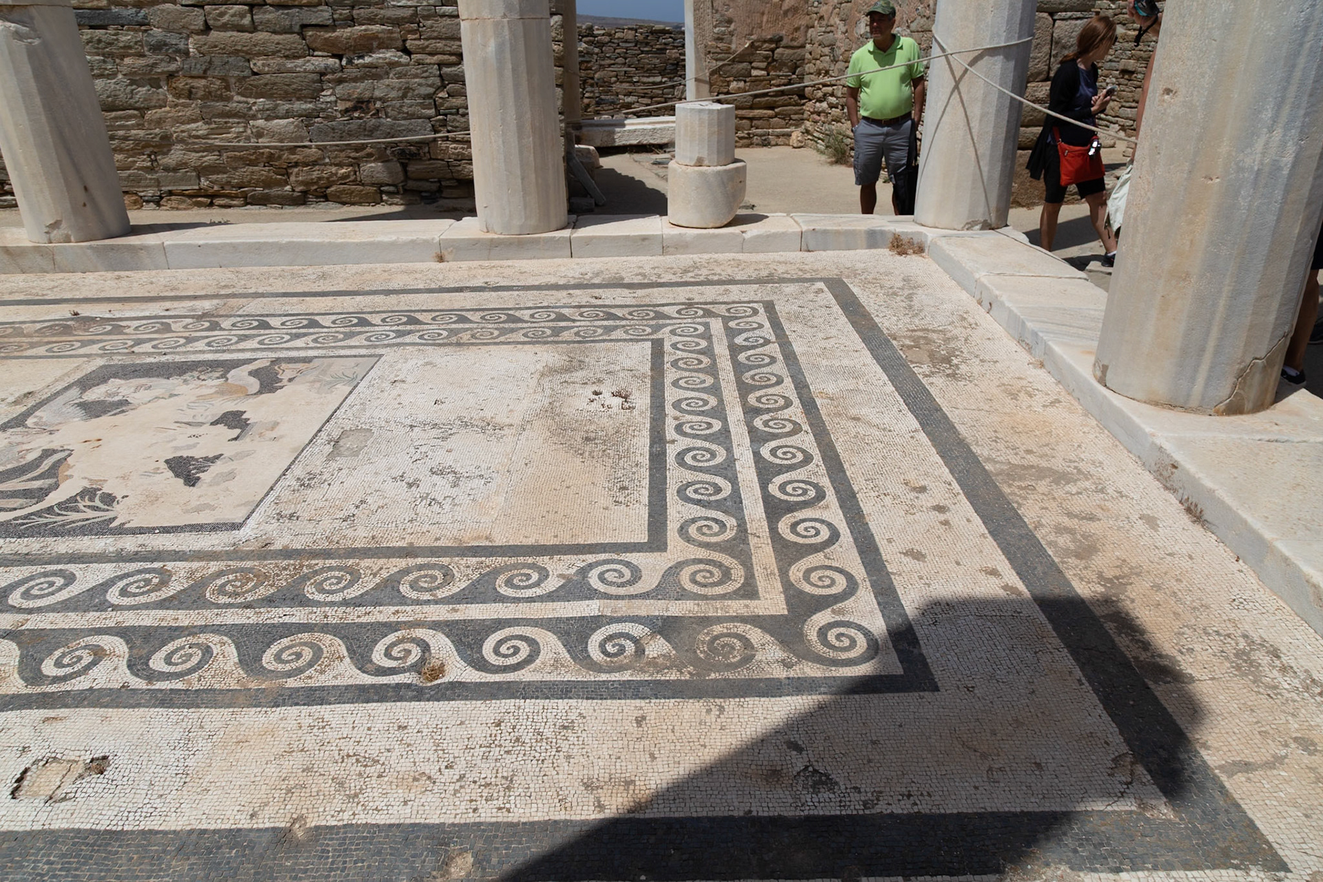 Delos, Greece - May 22nd 2018: Tourists admire the mosaic floor in the House of Dionysus. The mosaic depicts Dionysus riding a panther, a testament to the island's rich history.