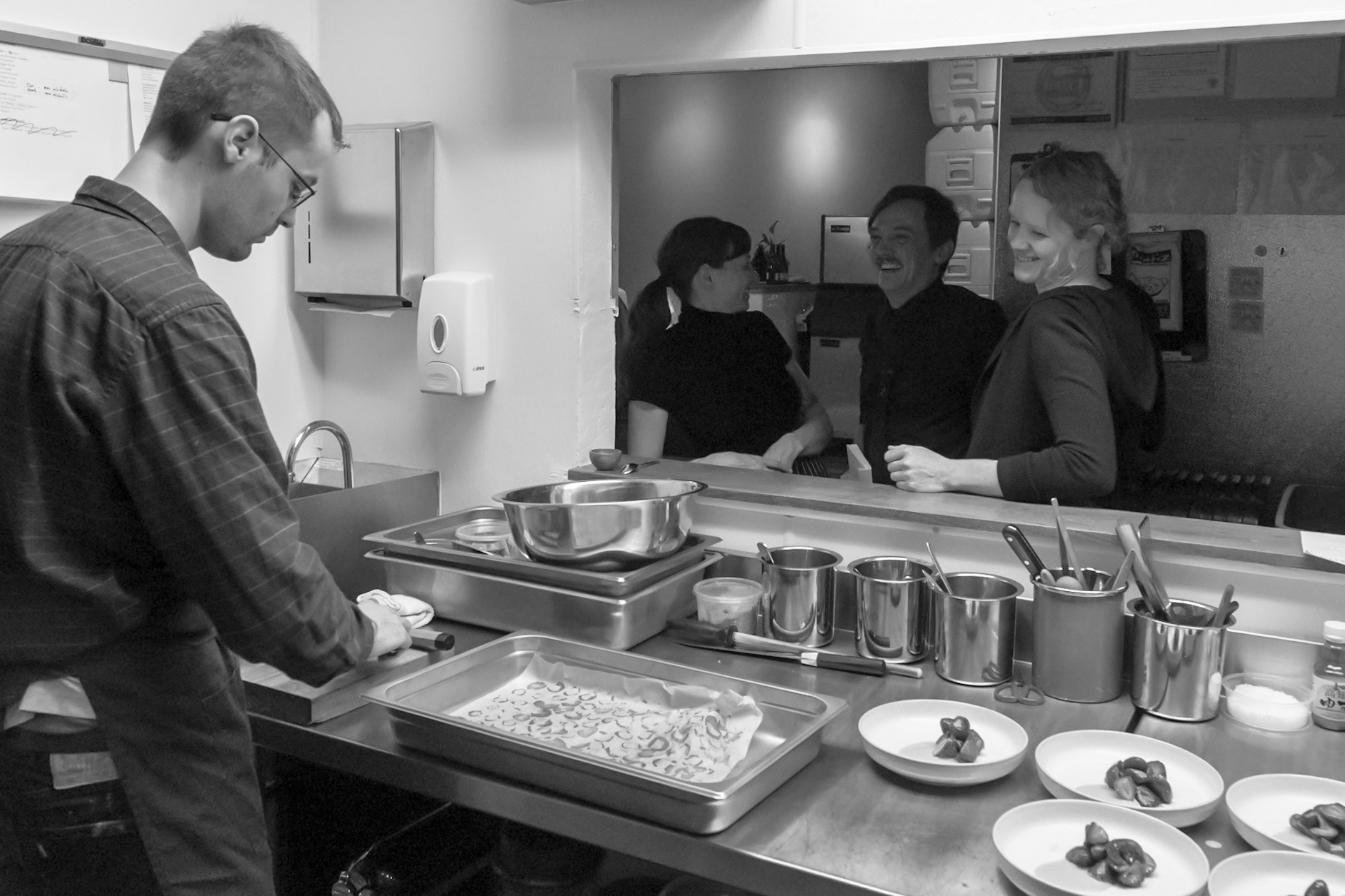 Fog Lark, Portland, Oregon - April 6th 2018: Chefs prep and plate food in a busy kitchen, while others chat through a service window.