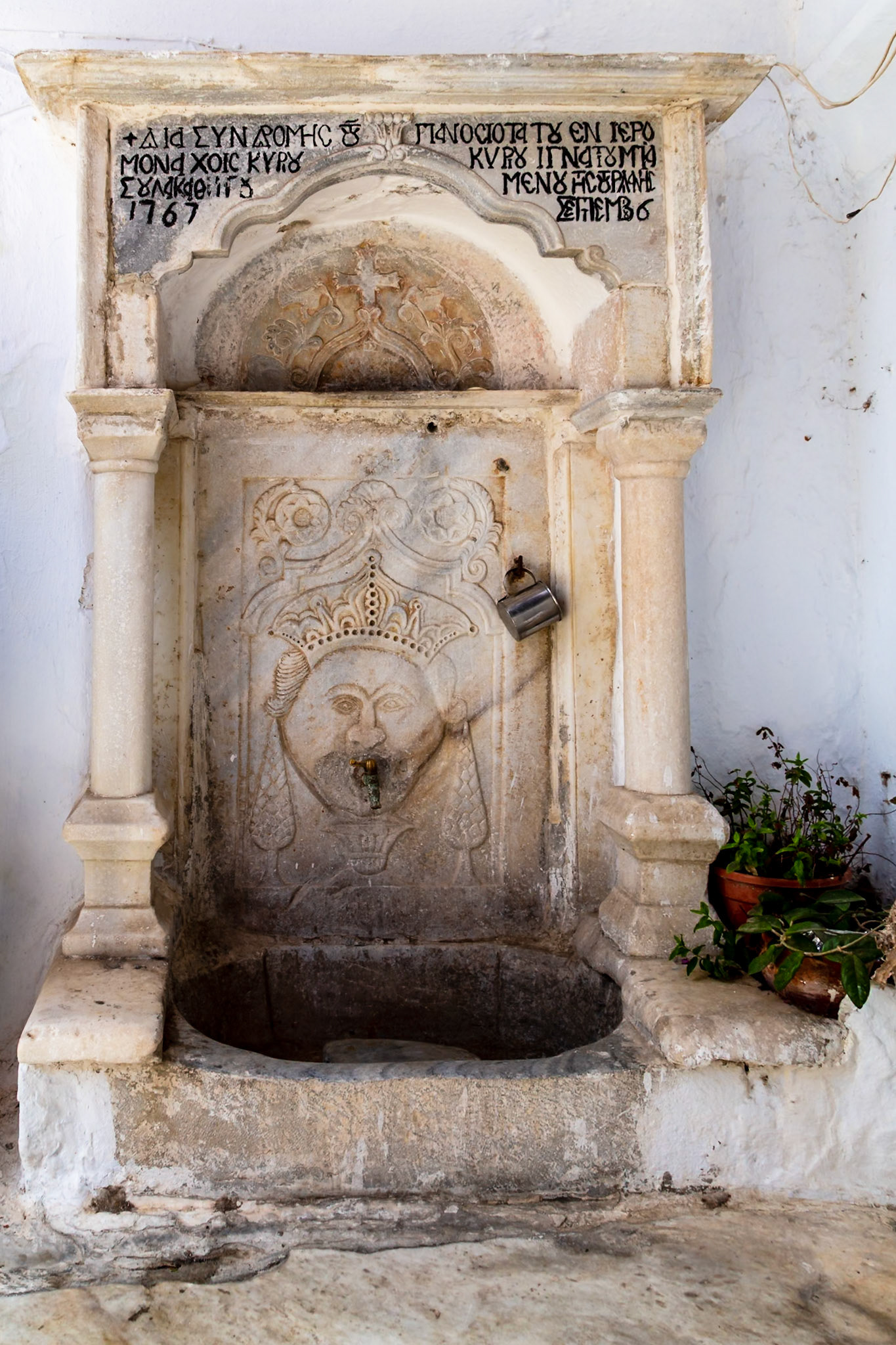 Mykonos, Greece - May 22nd 2018: An old stone water fountain with Greek inscriptions, built in 1767, stands as a testament to the island's history.