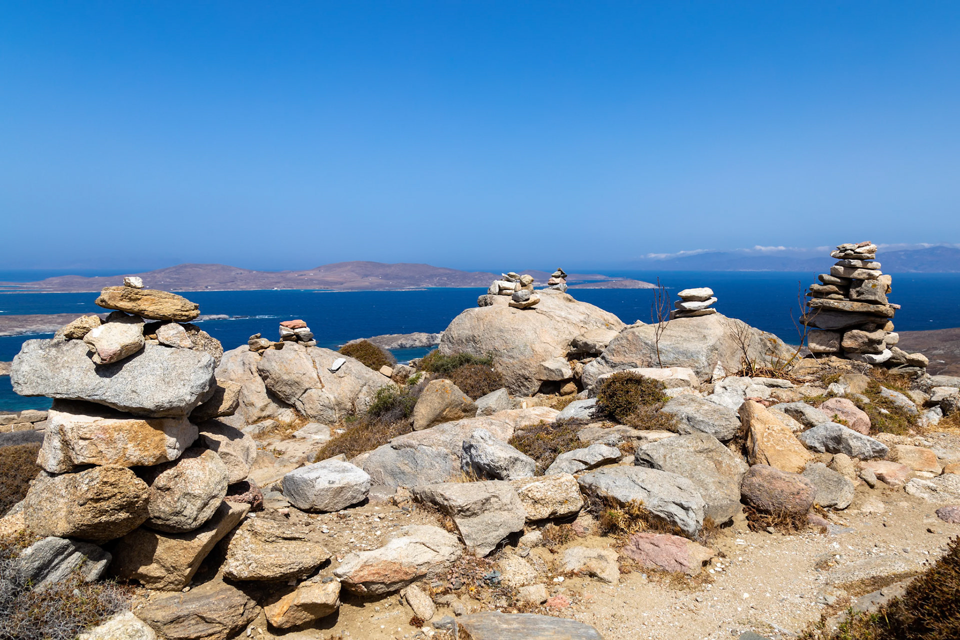 Delos, Greece - May 22nd 2018: Rock cairns stand on a hill overlooking the Aegean Sea. These structures are built by visitors to mark their passage and enjoy the view.