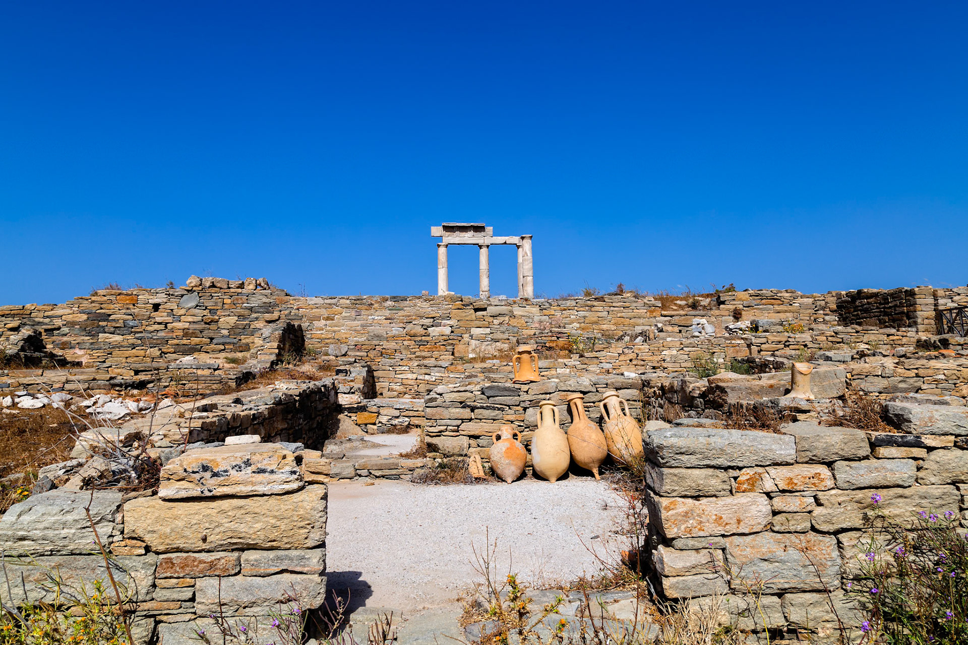 Delos, Greece - May 22nd 2018: Ancient ruins of Delos, a Greek island and archaeological site, featuring stone walls, amphorae, and the iconic Temple of Apollo.