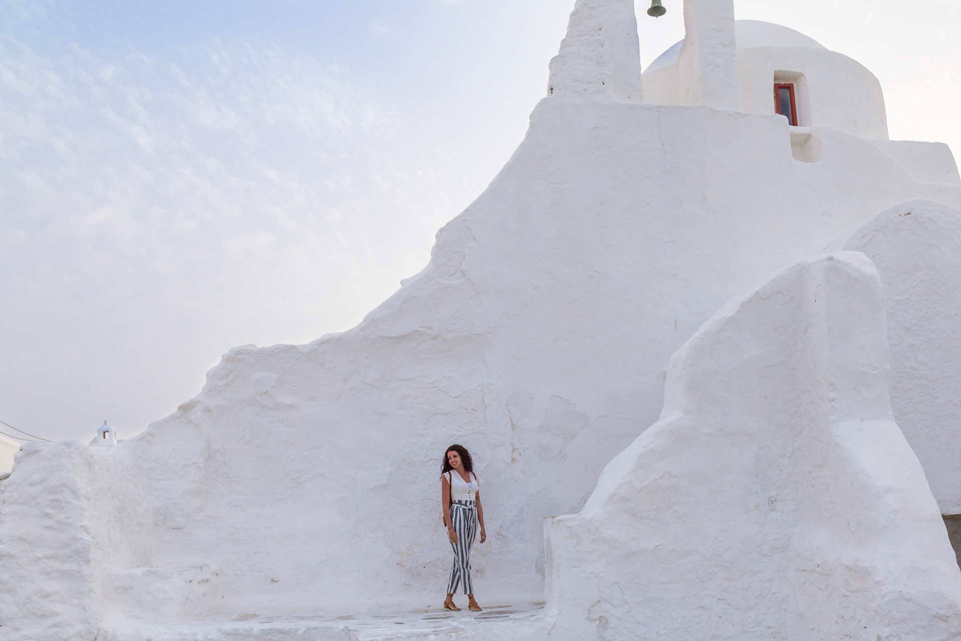 Mykonos, Greece - May 23rd 2018: A woman poses by the iconic whitewashed Paraportiani Church, capturing its unique architecture and charm.