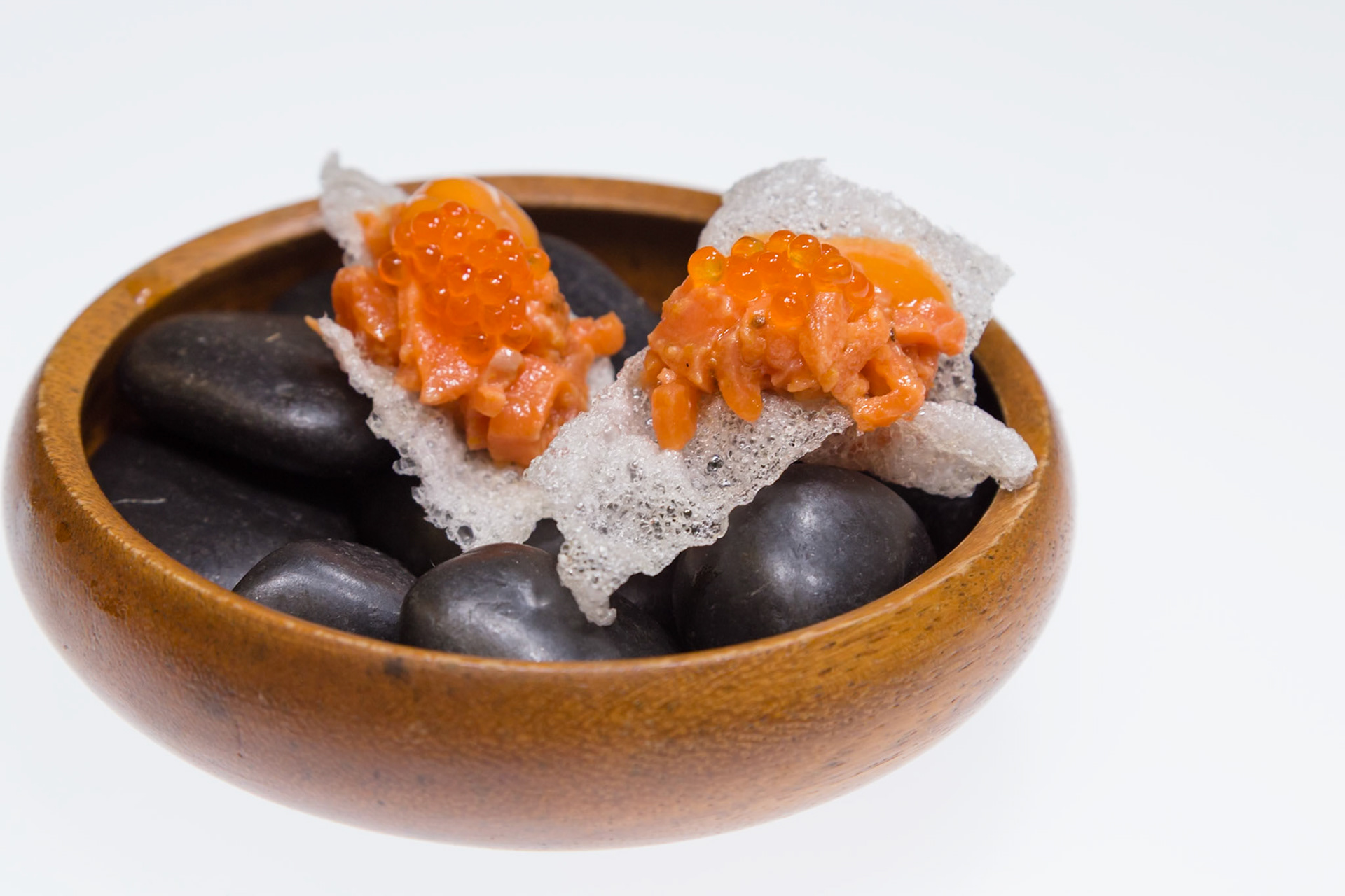 Fog Lark, Portland, Oregon - April 6th 2018: Salmon roe atop a crispy base sits in a wooden bowl with black stones, a culinary delight.