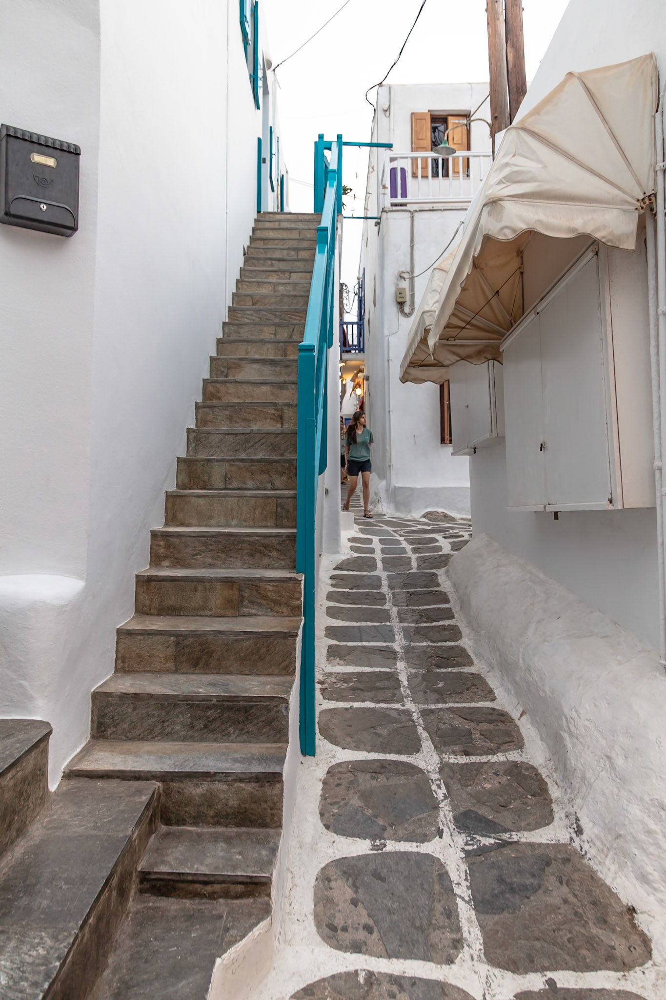 Mykonos, Greece - May 22nd 2018: A tourist walks along a narrow, stone-paved street lined with white buildings, exploring the island's unique architecture.