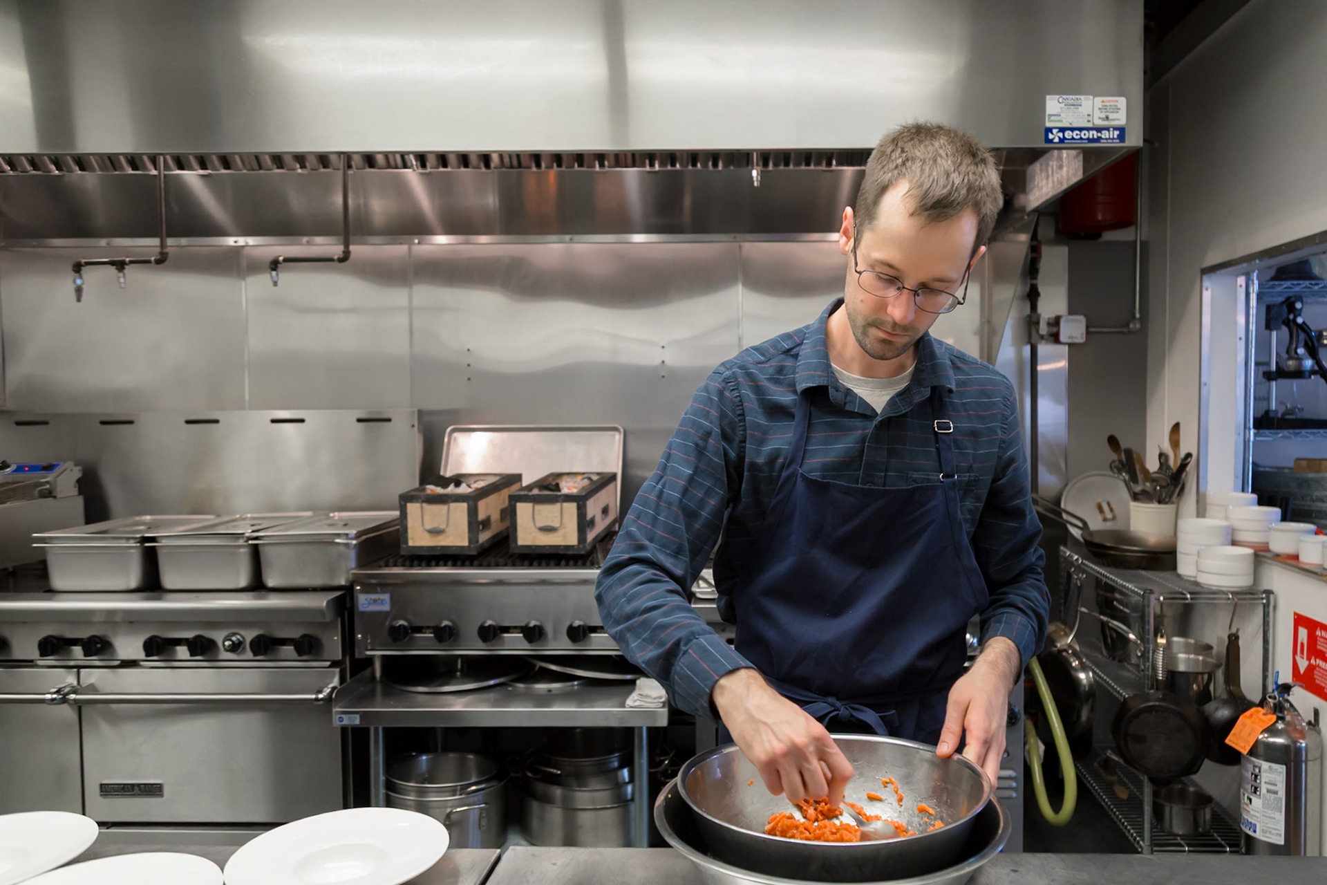 Fog Lark, Portland, Oregon - April 6th 2018: A chef in a commercial kitchen prepares food in a metal bowl, likely for a restaurant.
