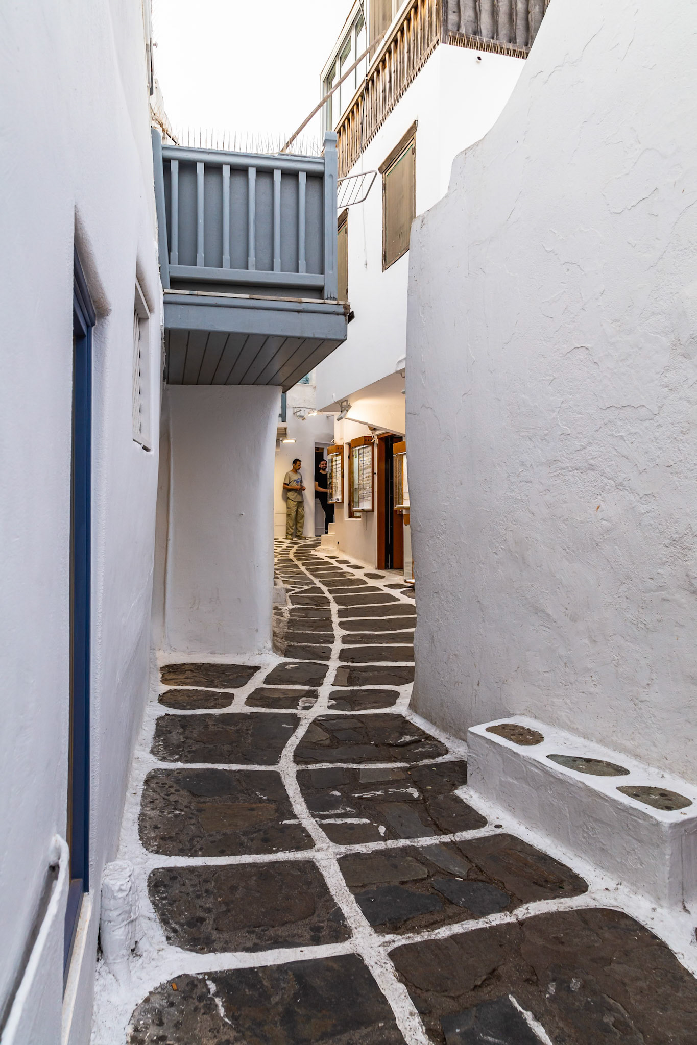 Mykonos, Greece - May 23rd 2018: Two people stand outside a shop on a narrow street paved with stone in Mykonos, Greece.