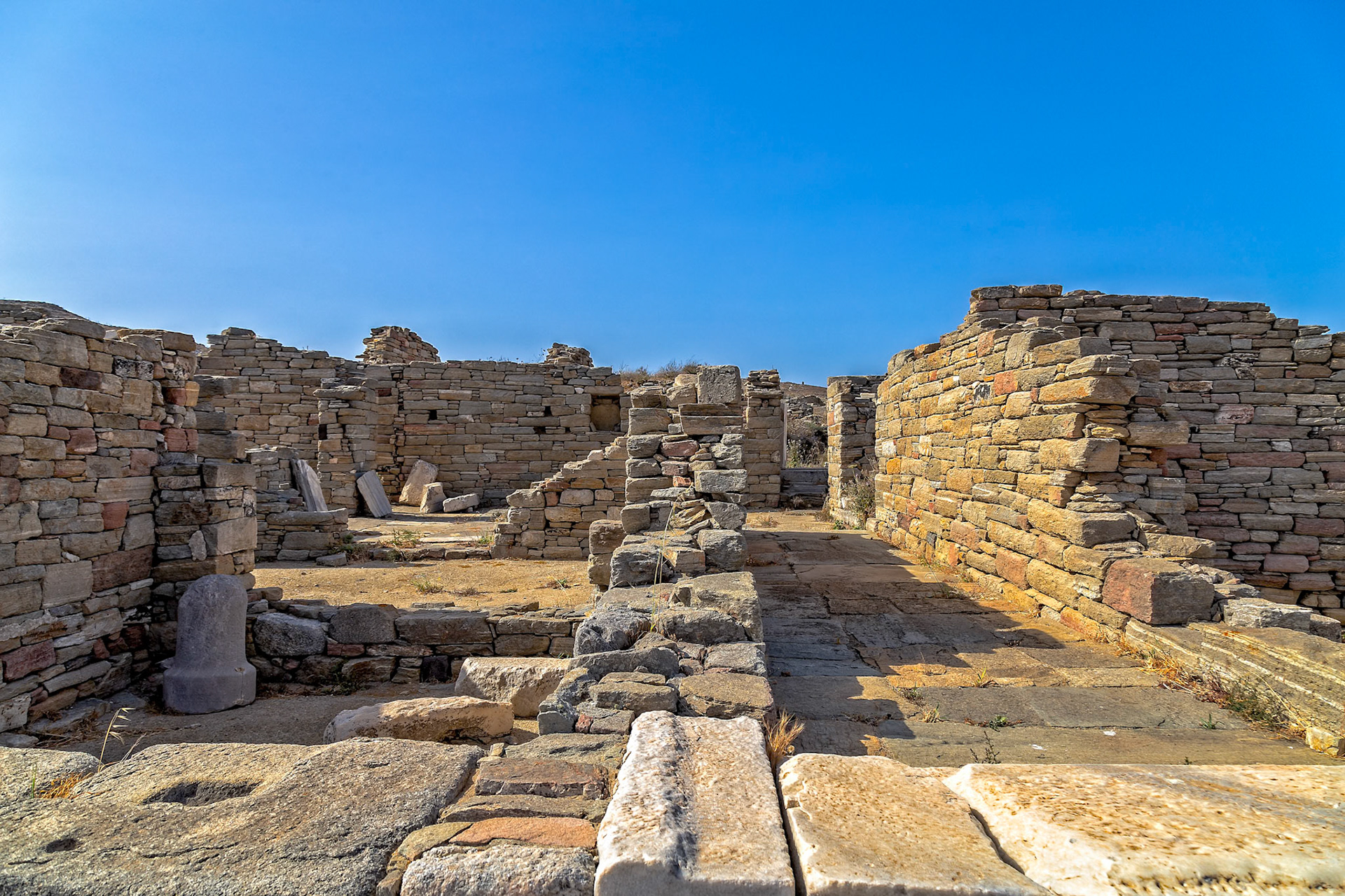 Delos, Greece - May 22nd 2018: Ancient ruins stand against a clear blue sky, showcasing the historical significance of Delos as a UNESCO World Heritage site.