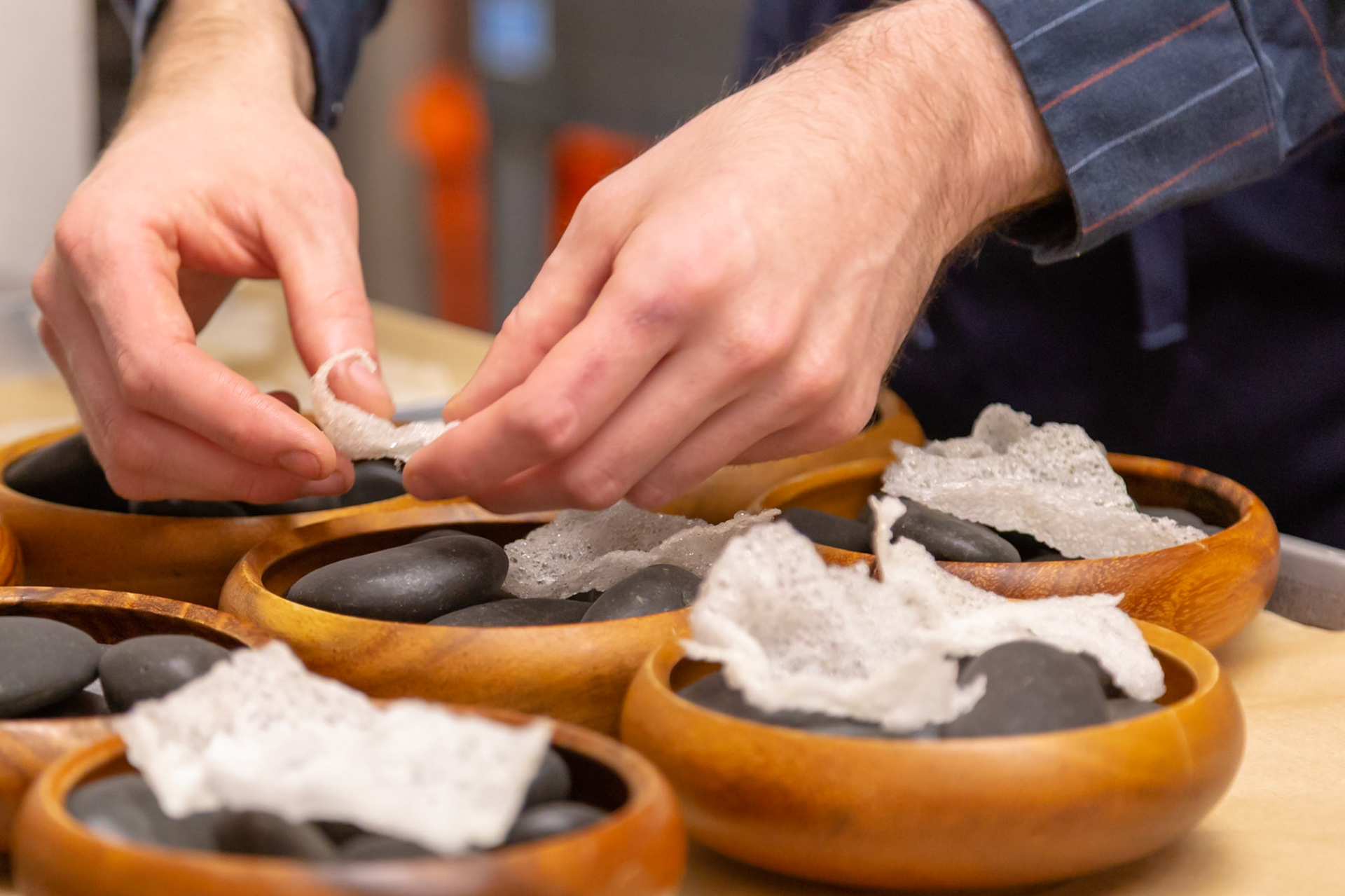 Fog Lark, Portland, Oregon - April 6th 2018: A chef delicately places a crispy garnish atop smooth stones in wooden bowls, adding a final touch to the dish.