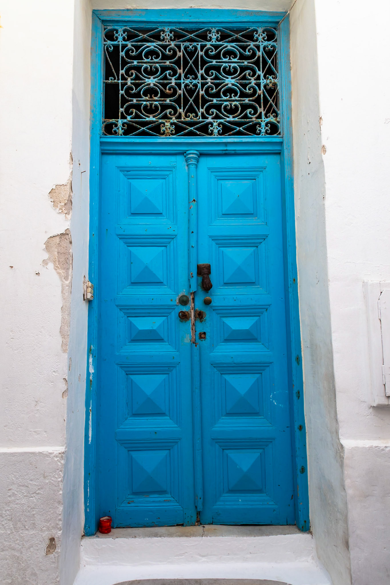 Mykonos, Greece - May 23rd 2018: A vibrant blue door with intricate ironwork stands out against the whitewashed walls of a traditional Mykonian building.