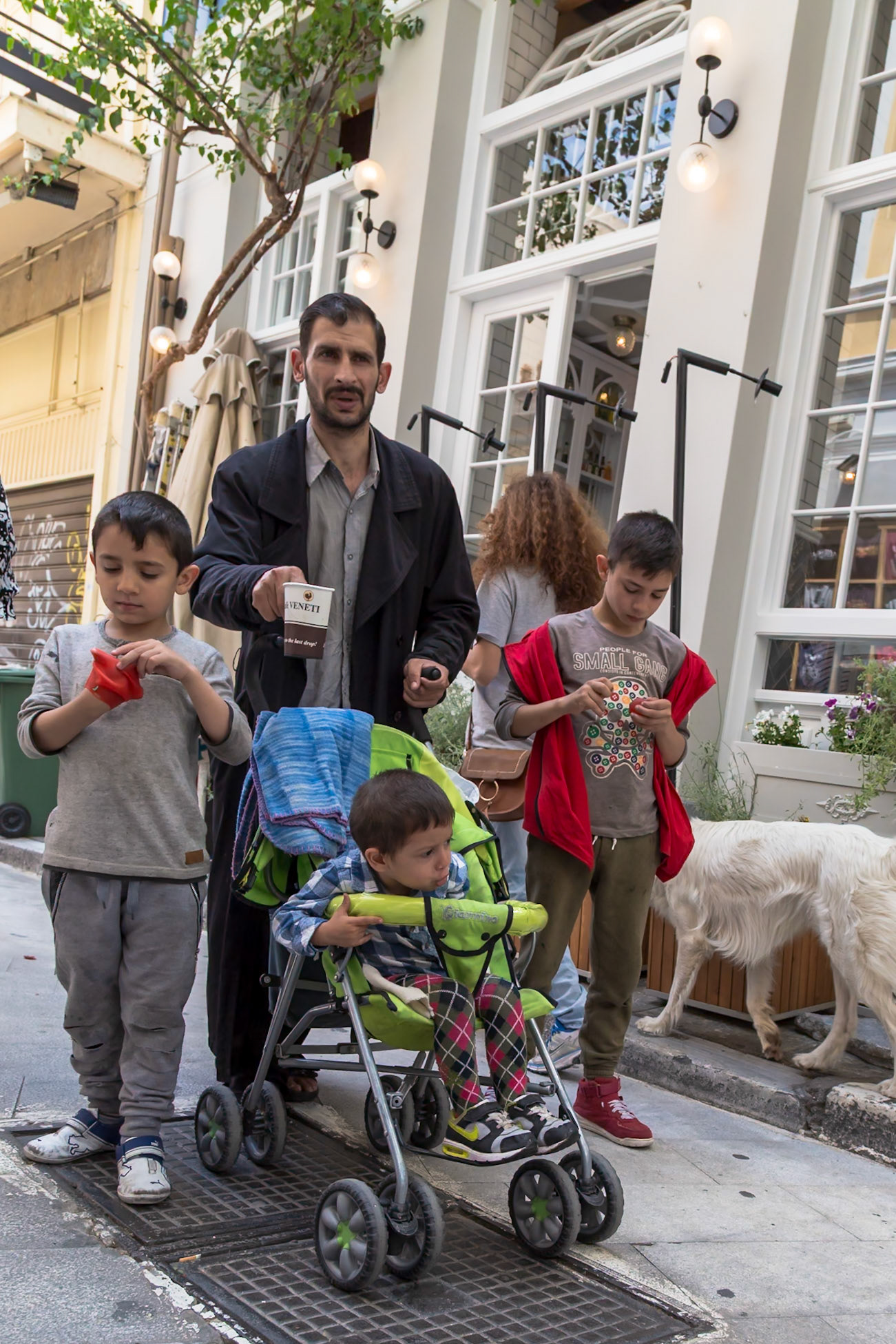 Athens, Greece - May 23rd 2018: A man stands with his three children, one in a stroller, on a city street, possibly on their way to or from an outing.