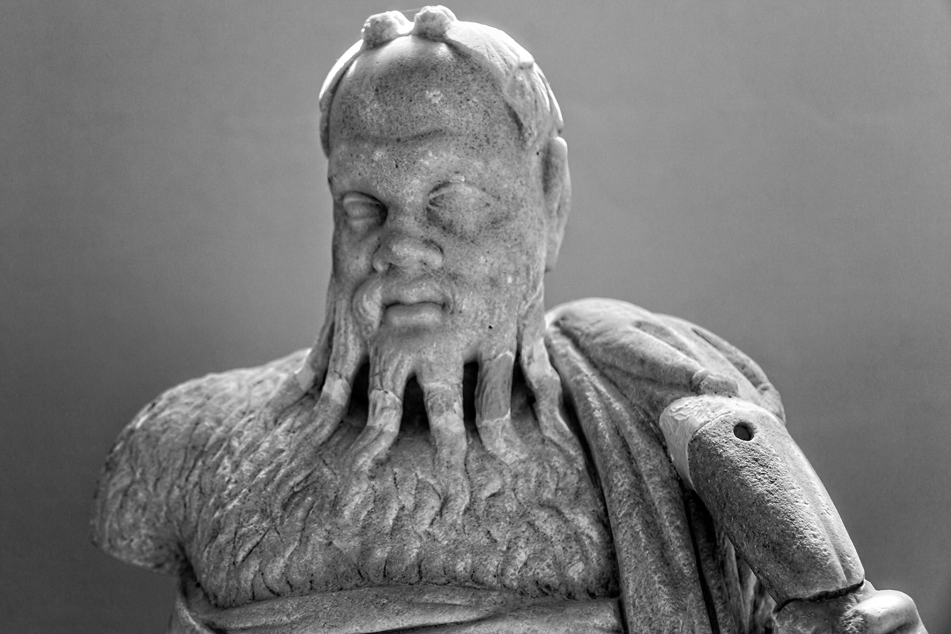 Delos, Greece - May 22nd 2018: A weathered statue of Poseidon stands, his beard formed of octopus tentacles, a testament to the island's rich mythological past.