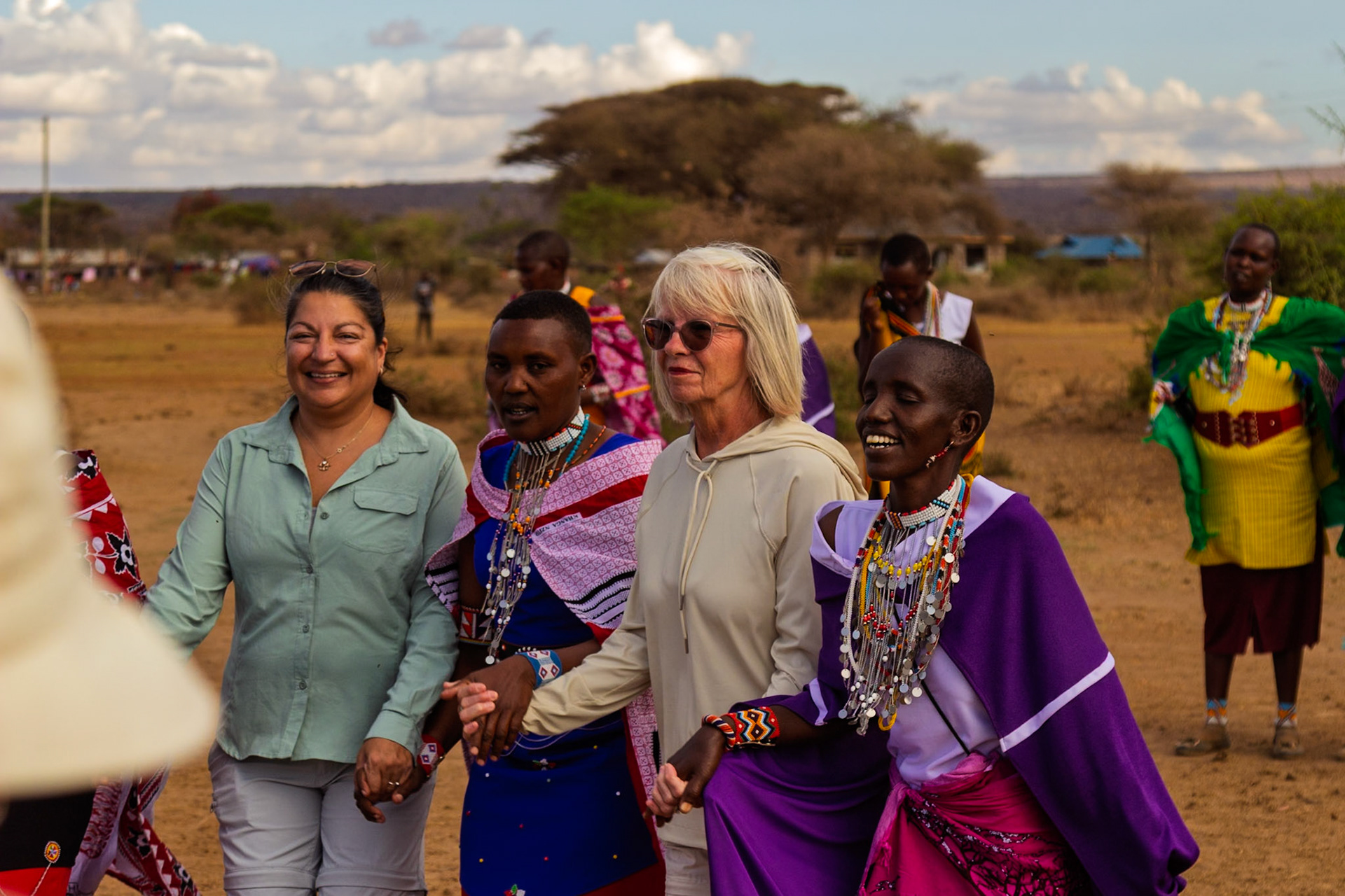 Tourists hold hands with Maasai women in Kenya, experiencing local culture and traditions in a vibrant village setting.