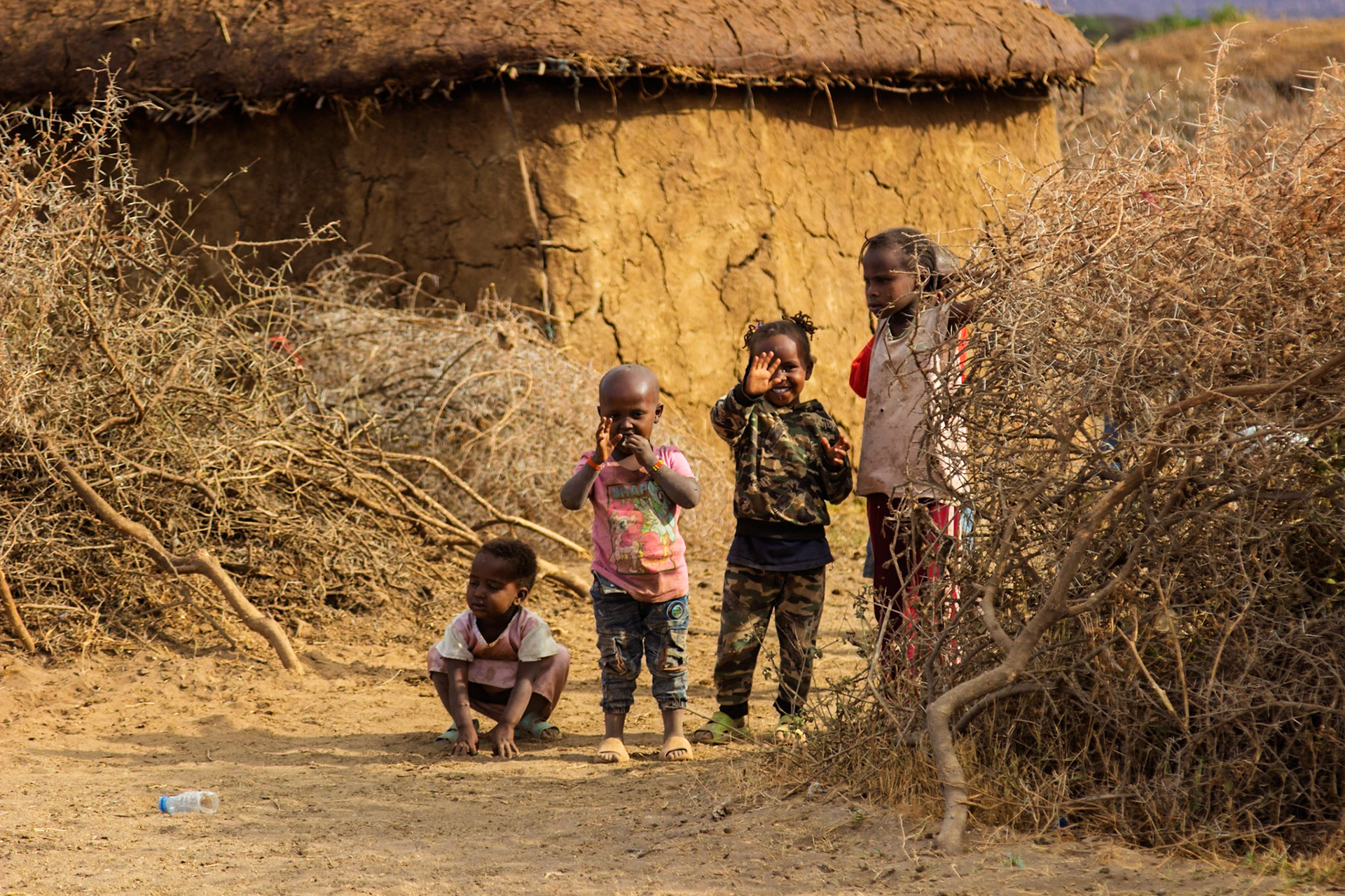 Maasai children play outside their home in a village in Kenya. They are smiling and enjoying the day.