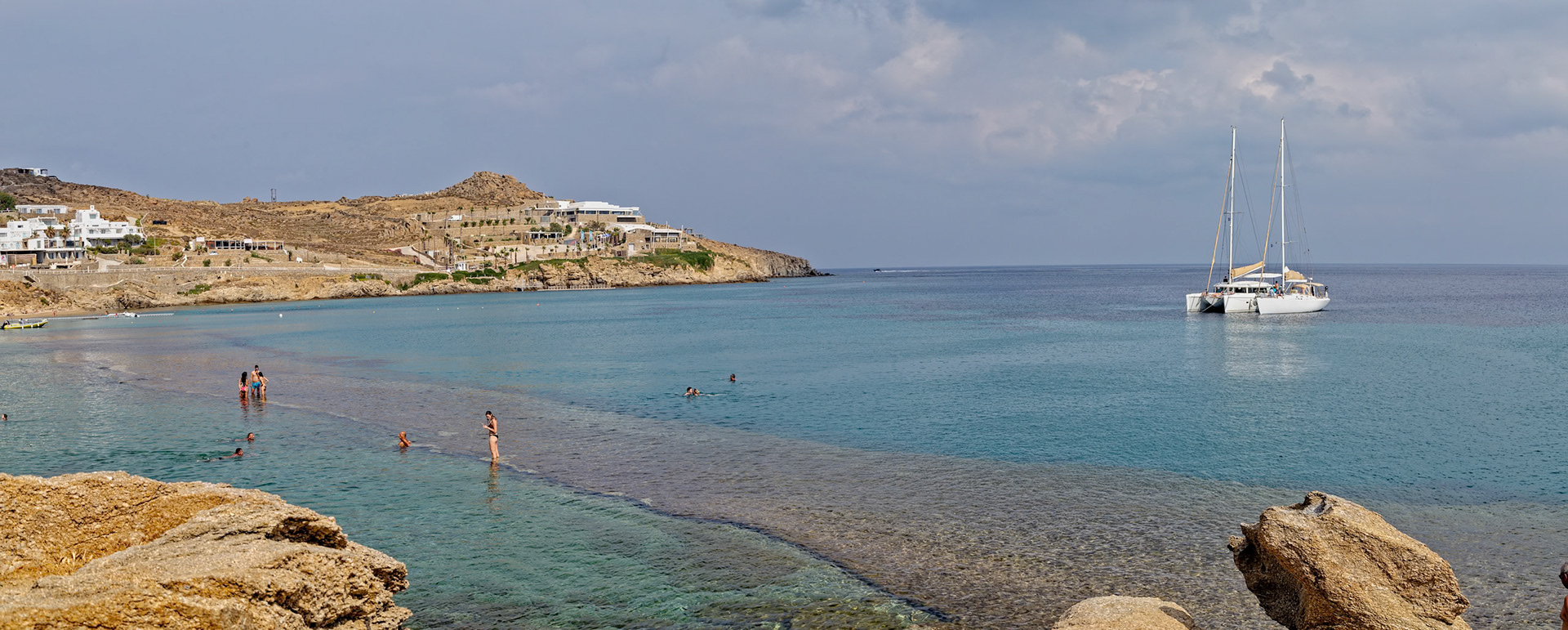 Paradise Beach, Mykonos, Greece - May 24th 2018: People are swimming and enjoying the clear water. A catamaran is anchored in the distance.