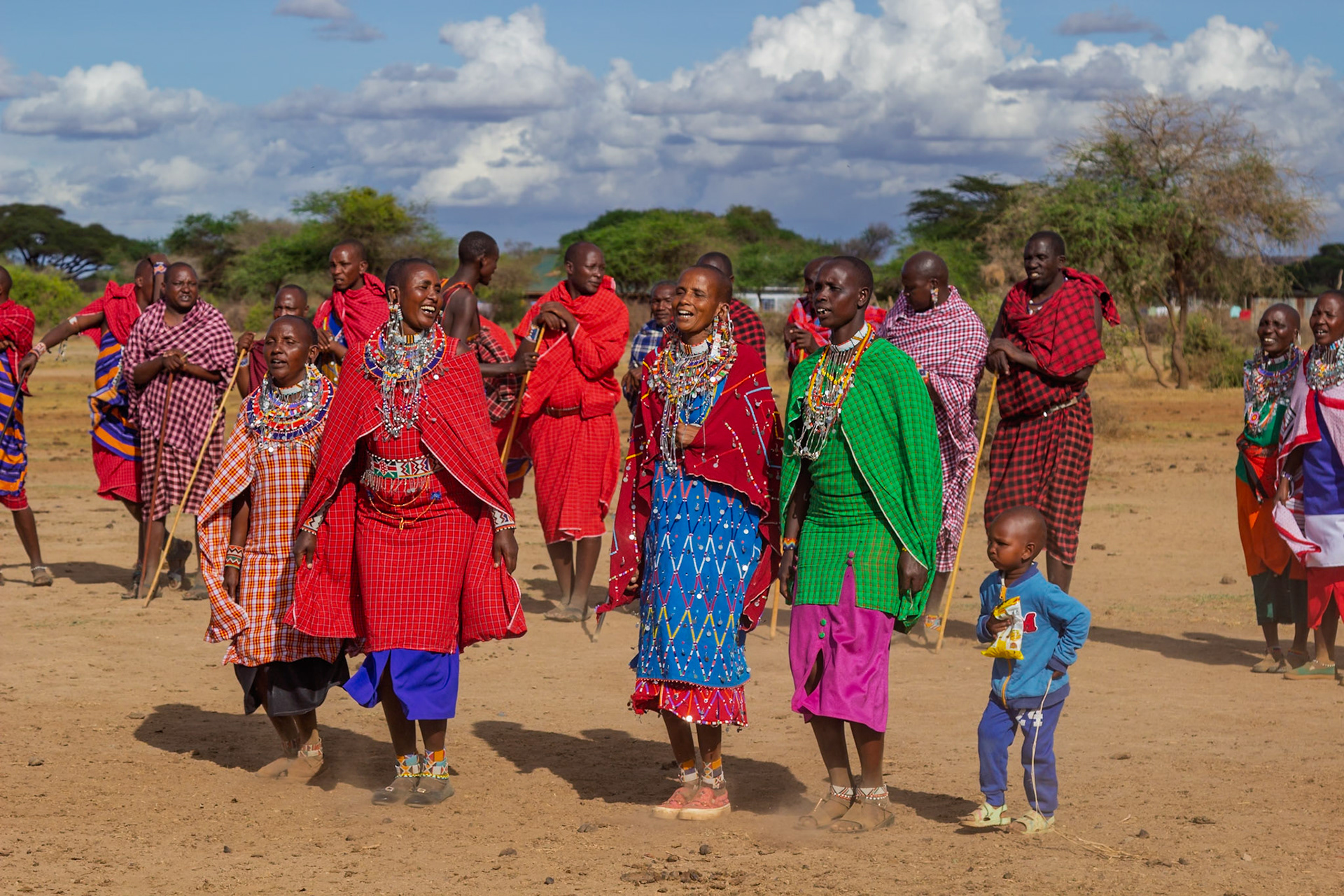 Maasai people in Kenya are celebrating in their village, wearing traditional clothing and jewelry.