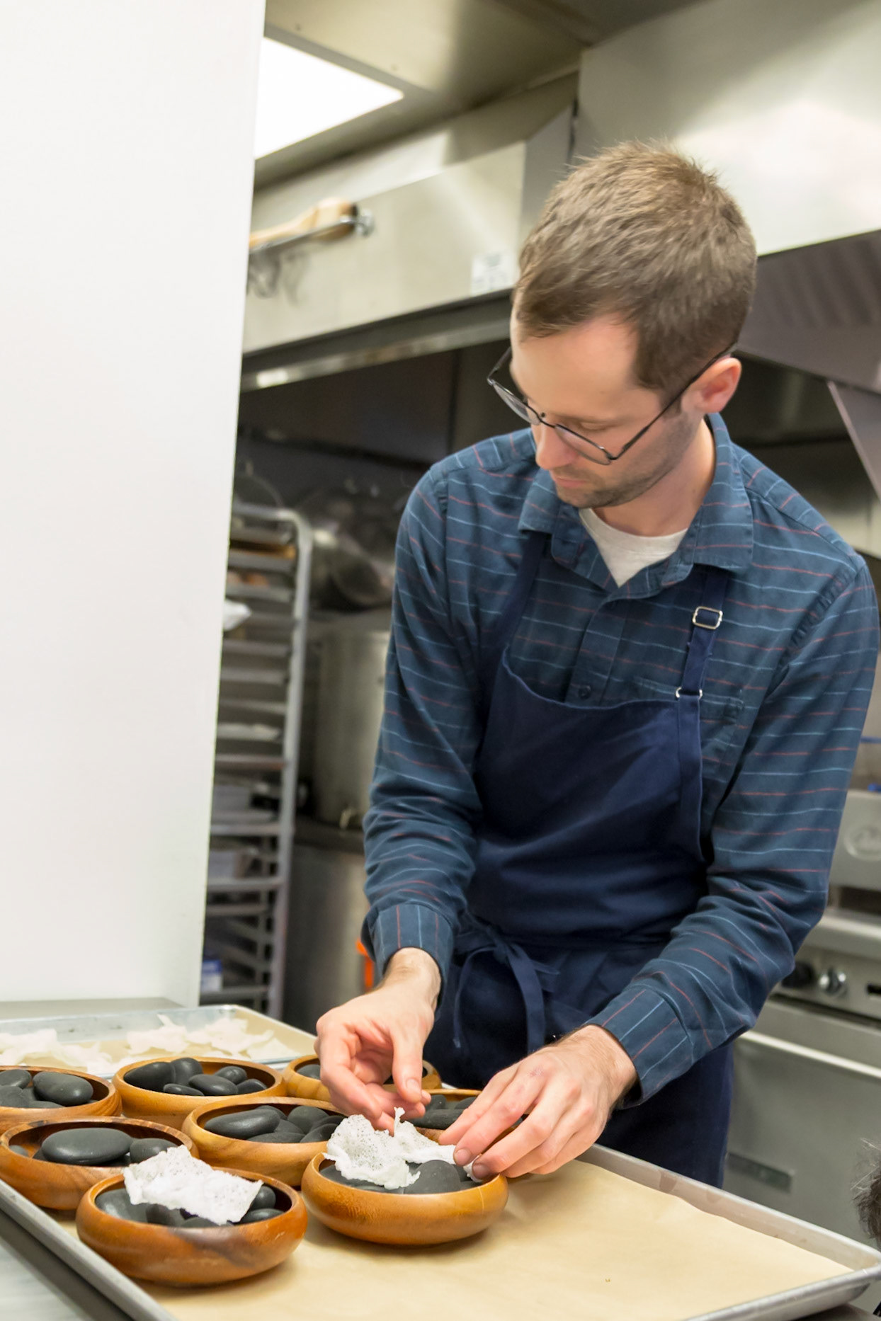 Fog Lark, Portland, Oregon - April 6th 2018: Chef is preparing a dish with black rocks and white paper in wooden bowls in a professional kitchen.