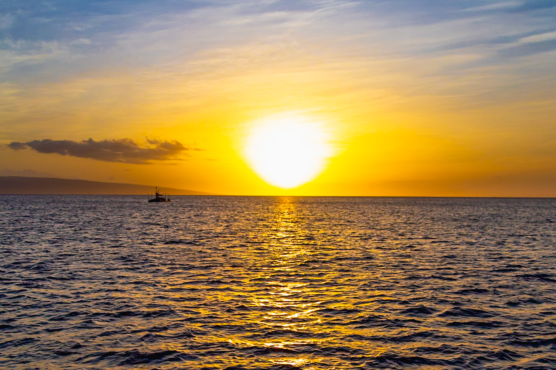 Maui, Hawaii, USA - April 7th 2022: A boat sits on the water as the sun sets over the Pacific Ocean, creating a golden glow.