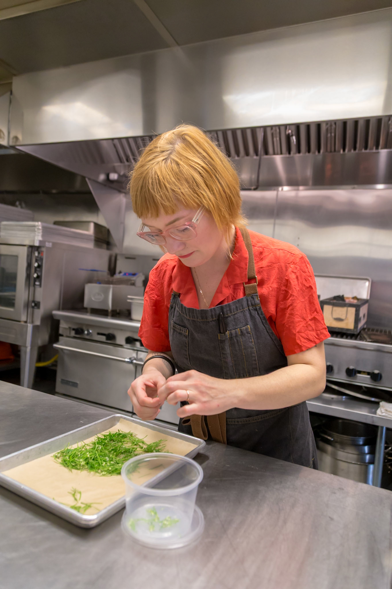 Fog Lark, Portland, Oregon - April 6th 2018: A chef in a red shirt and apron prepares greens on a baking sheet in a commercial kitchen.