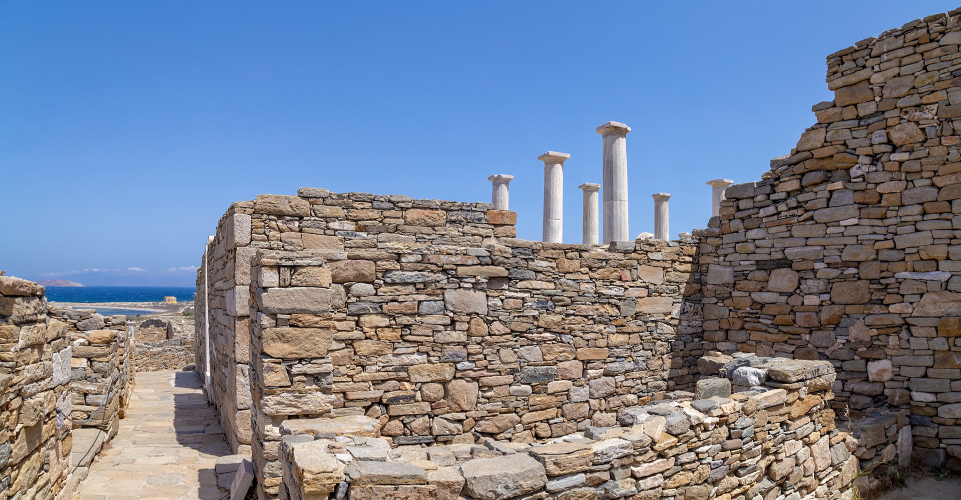 Delos, Greece - May 22nd 2018: Ancient ruins stand against a clear blue sky. The stone walls and columns are remnants of a once-thriving civilization.