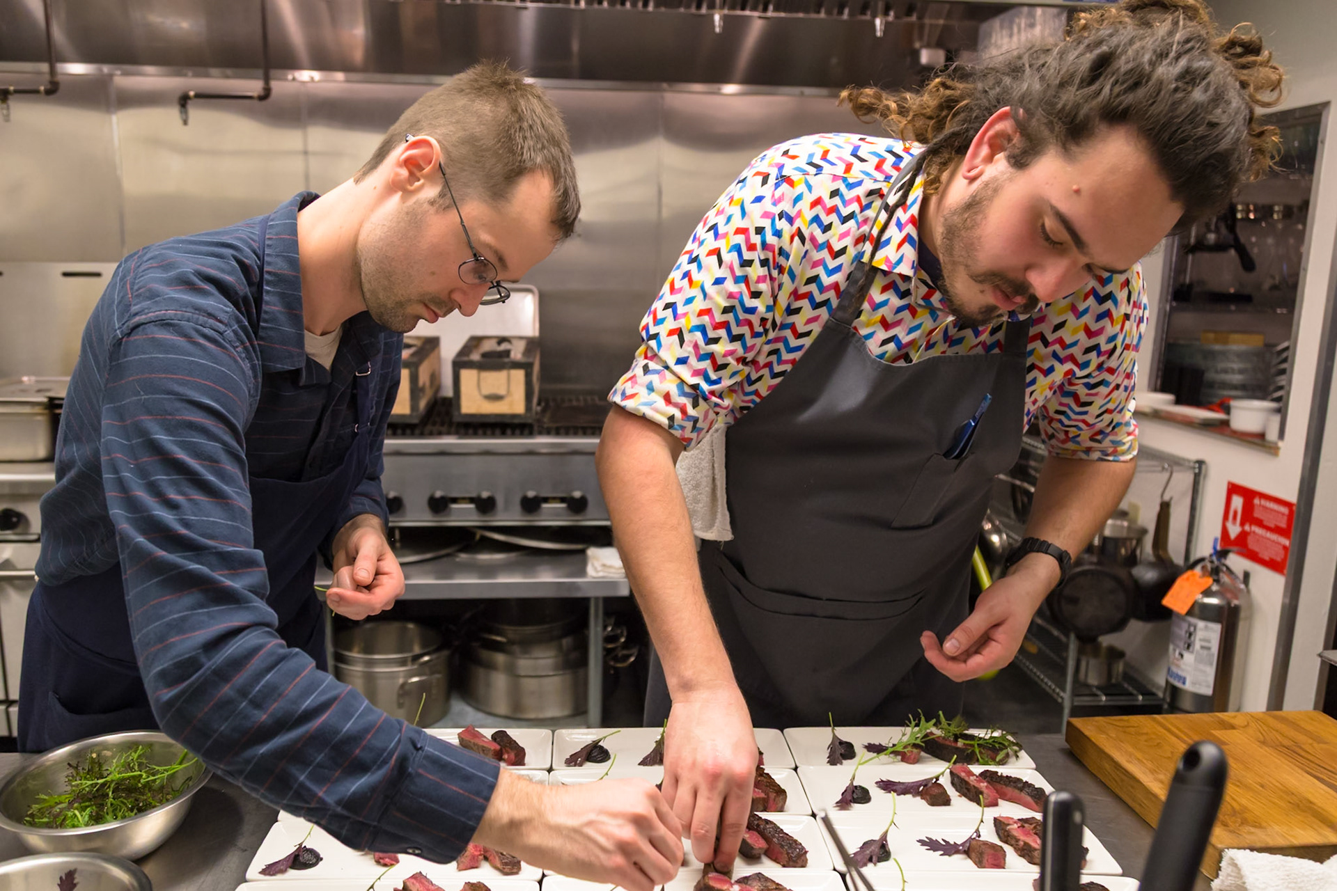 Fog Lark, Portland, Oregon - April 6th 2018: Two chefs plating a dish with sliced steak and greens in a professional kitchen.