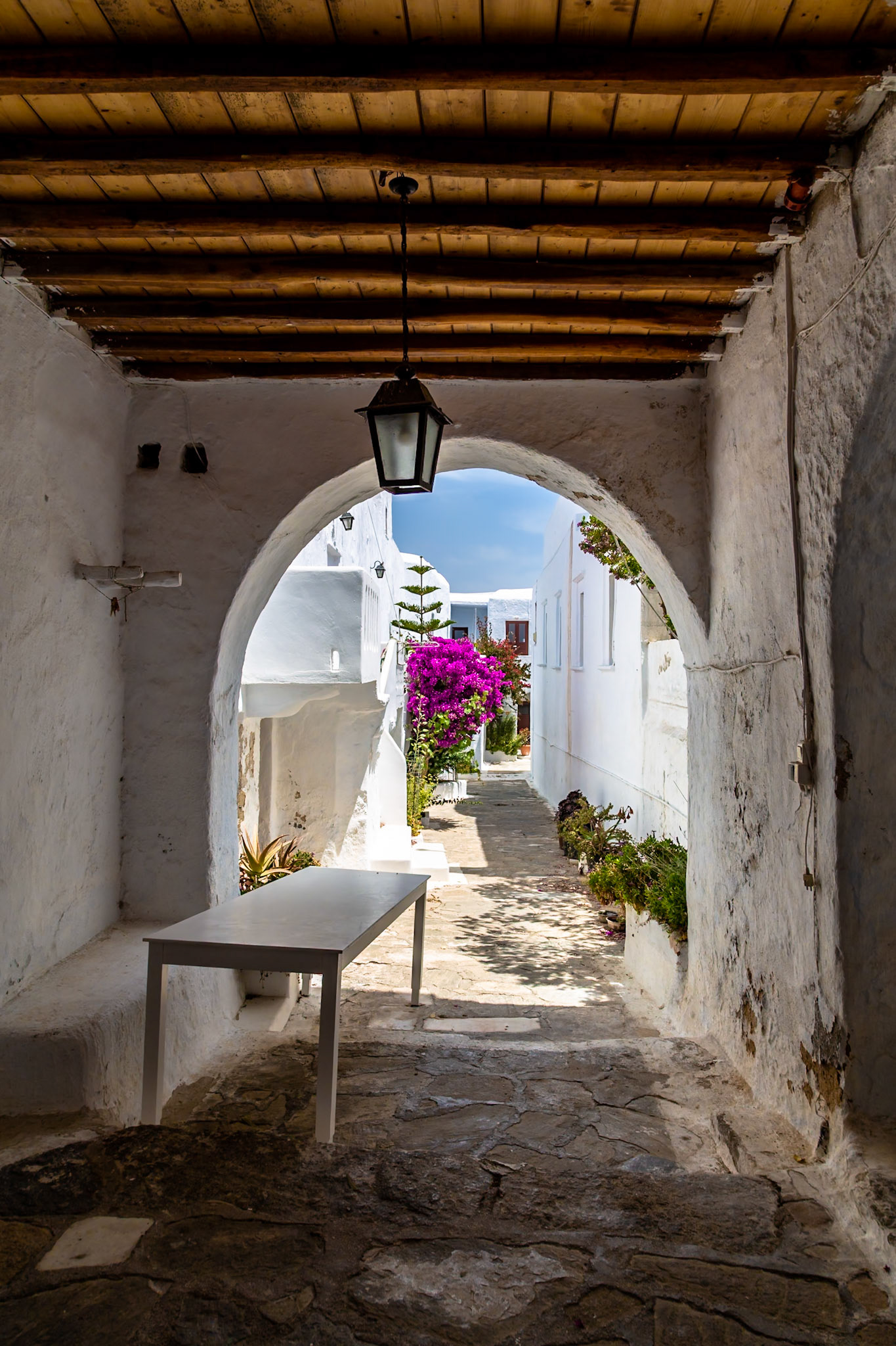 Mykonos, Greece - May 22nd 2018: A picturesque alleyway is framed by an archway, showcasing the island's iconic white buildings and vibrant bougainvillea.