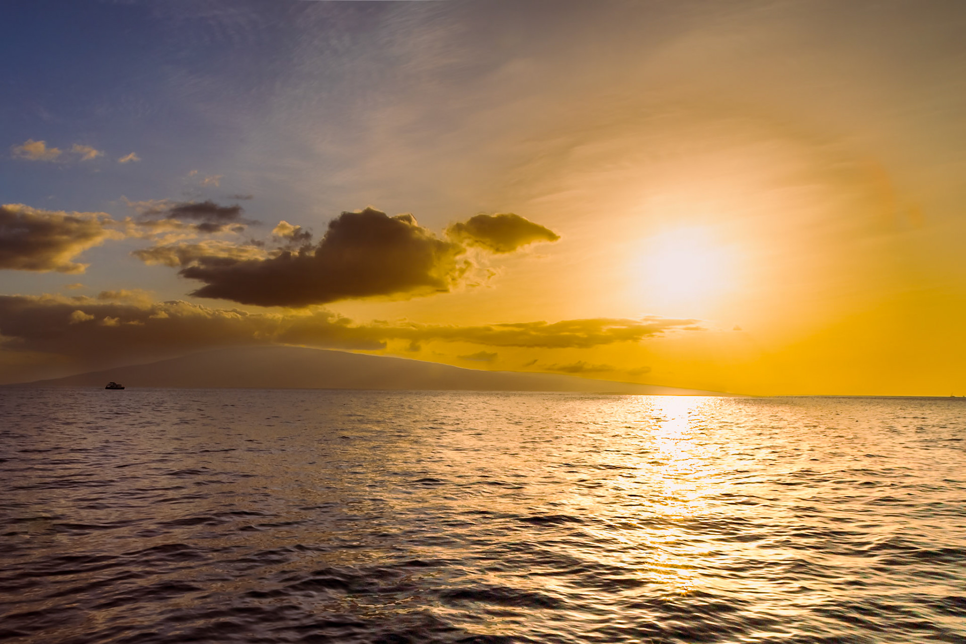 Maui, Hawaii, USA - April 7th 2022: A golden sunset over the ocean, with a boat sailing towards the island of Lanai in the distance.