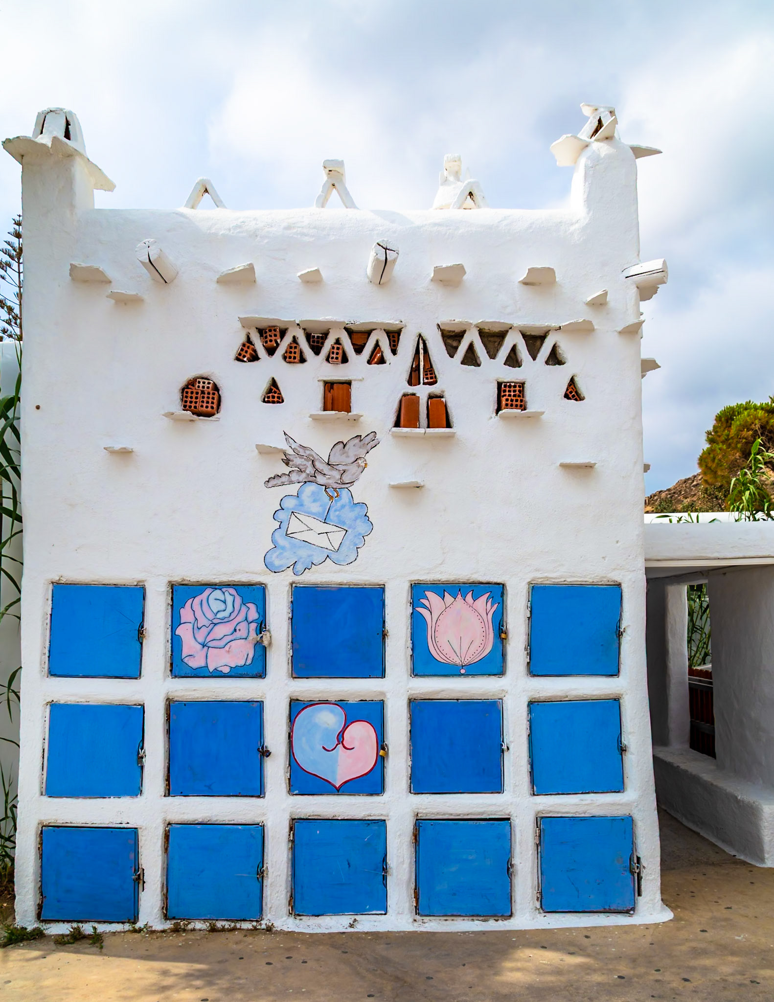 Paradise Beach, Mykonos, Greece - May 24th 2018: A white building with blue doors and painted flowers/heart, possibly a storage or decorative structure.
