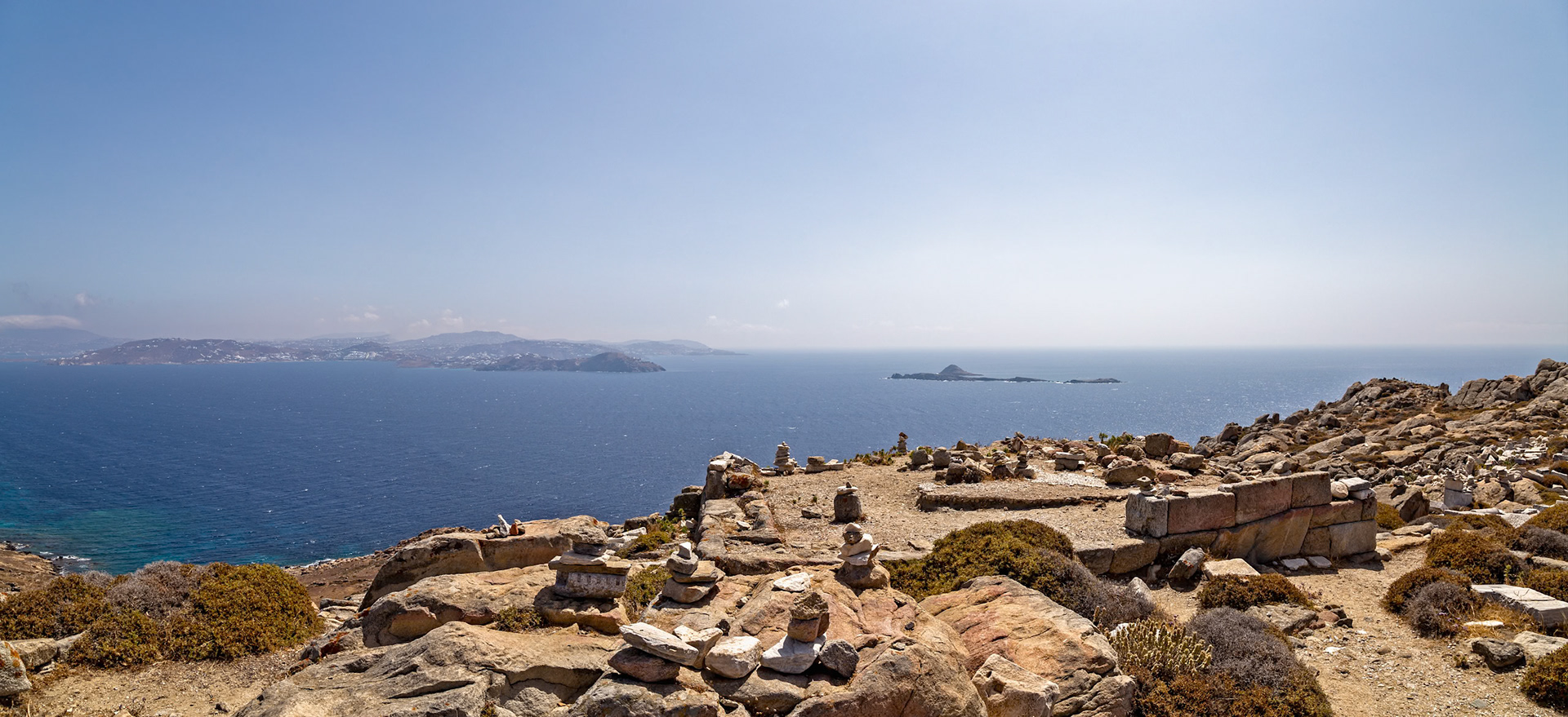 Delos, Greece - May 22nd 2018: A scenic view of the Aegean Sea from Delos, with stacked stones in the foreground, creating a serene and historical landscape.